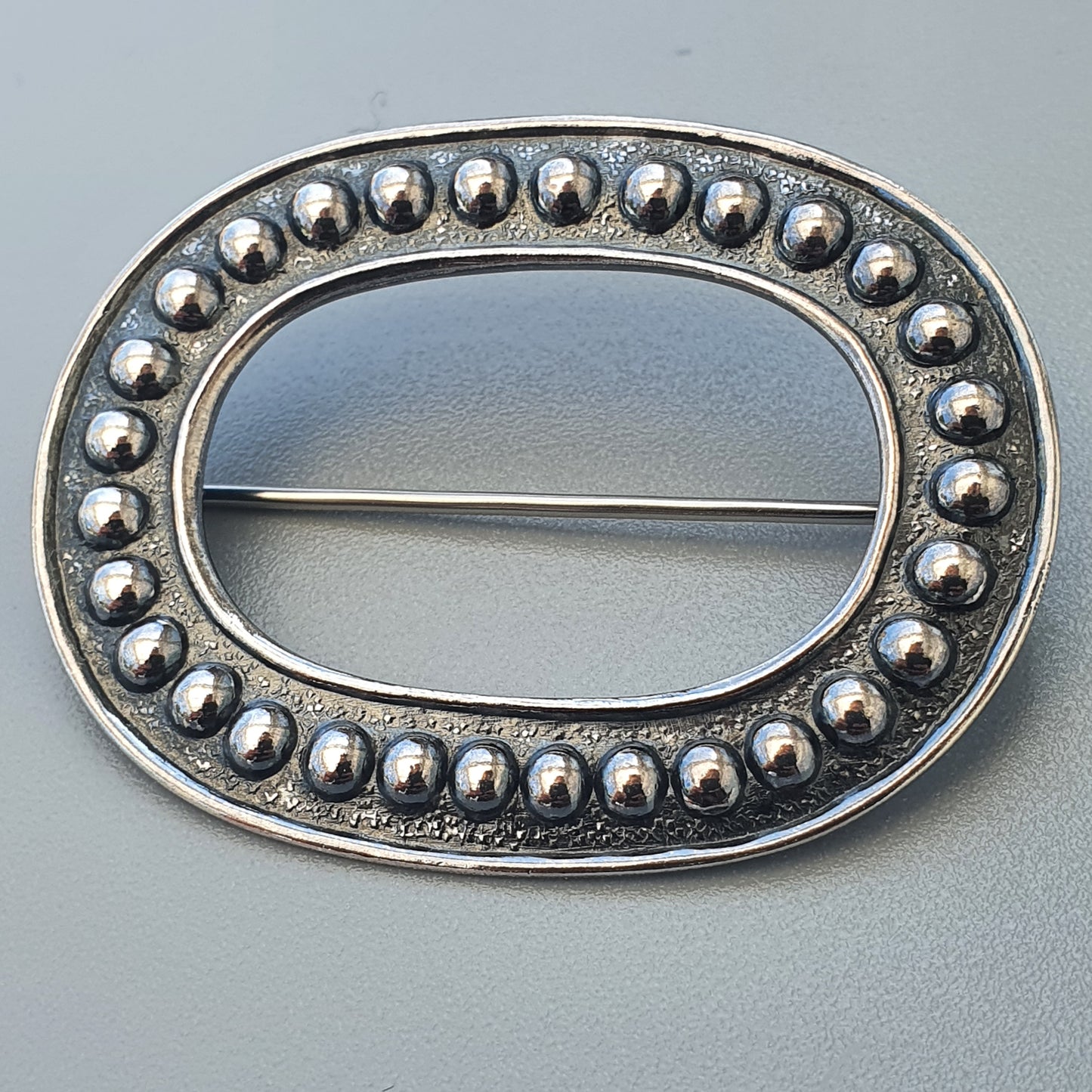 Oval silver brooch with beaded border design.