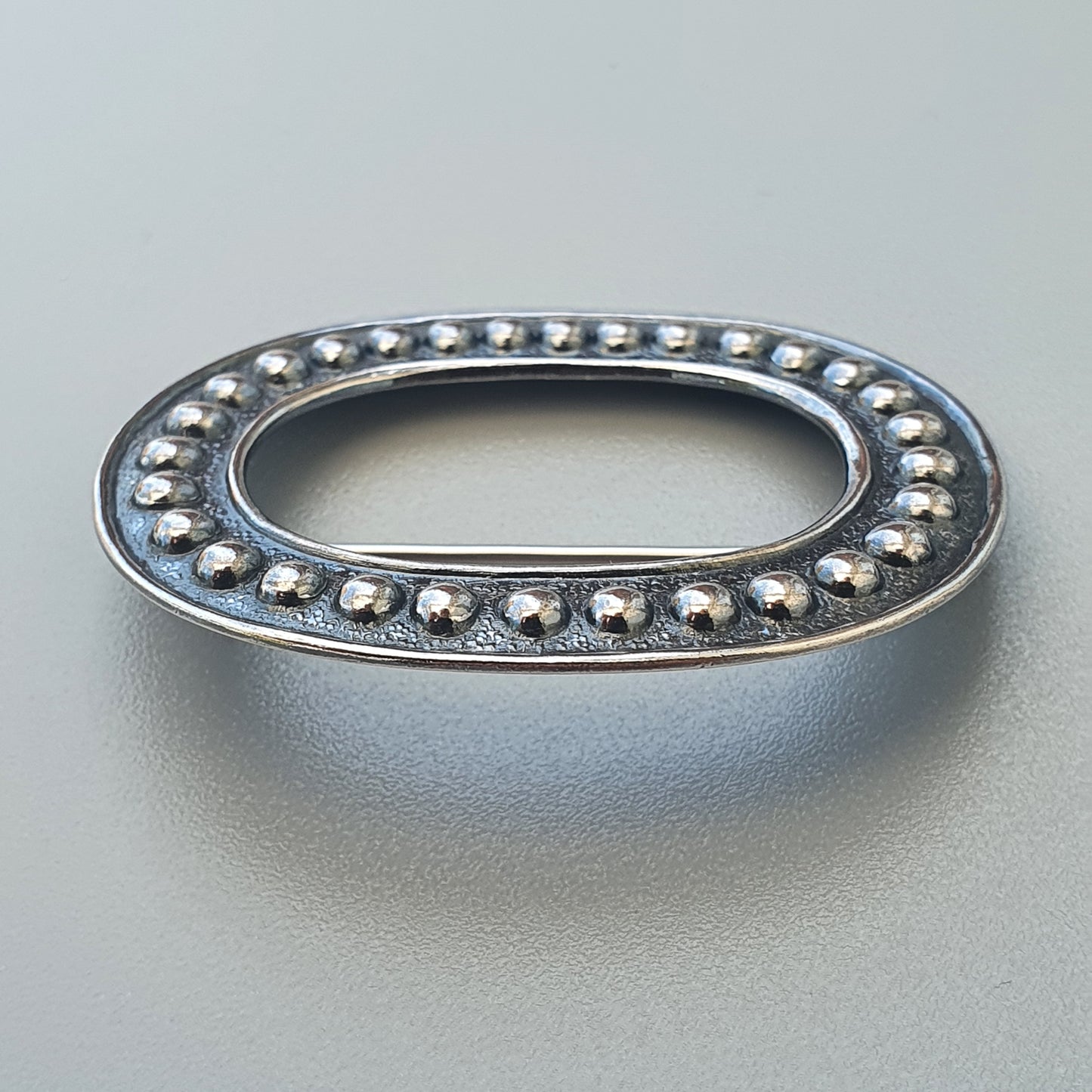 Oval-shaped silver metal ring or frame adorned with small beads around its perimeter.