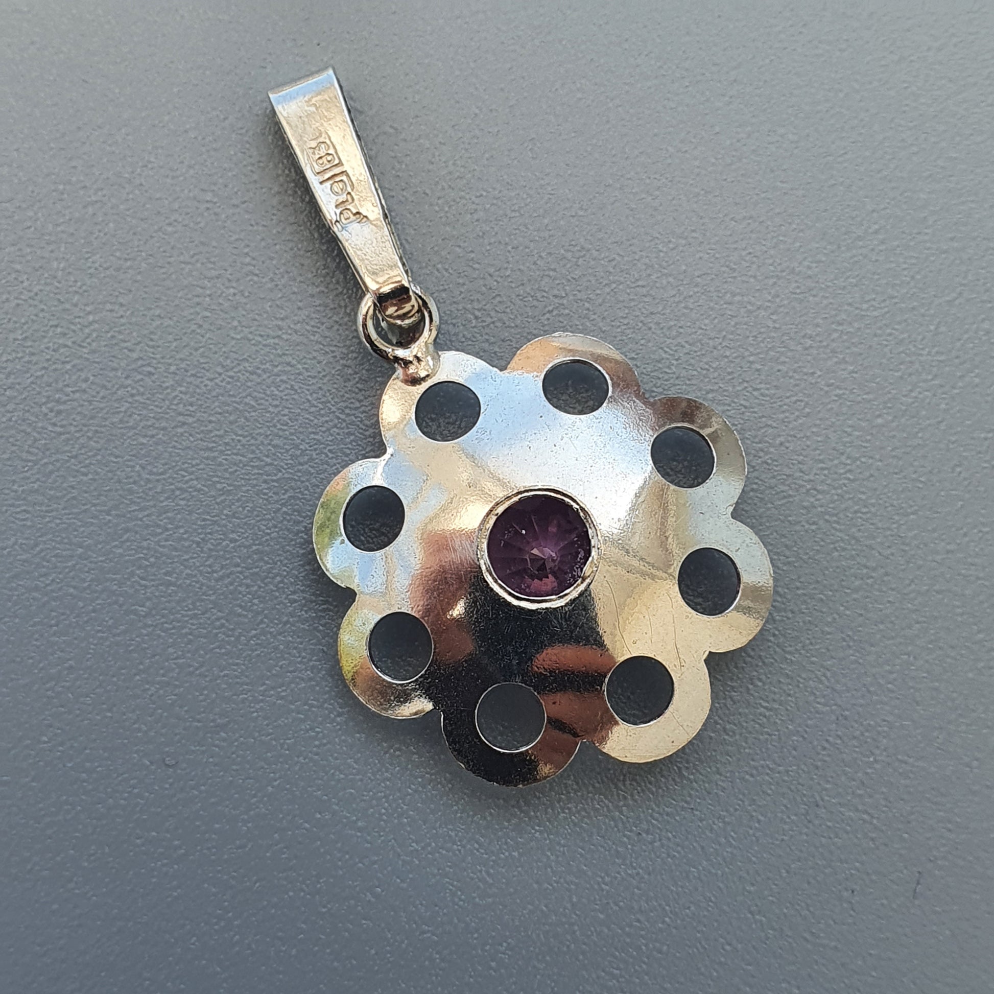 Silver flower-shaped pendant with black polka dots and a purple gemstone center.