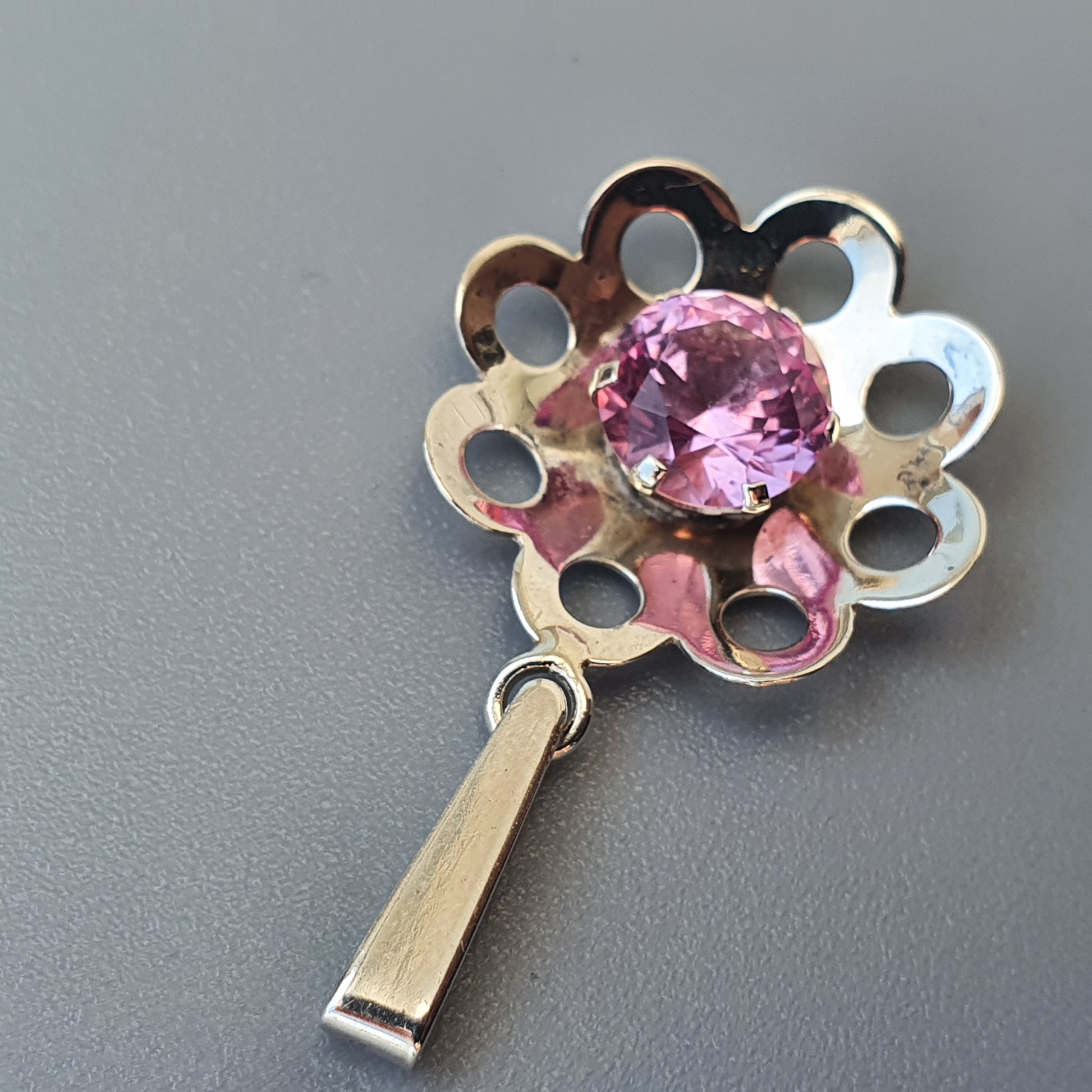 Flower-shaped silver pendant with a pink gemstone center.