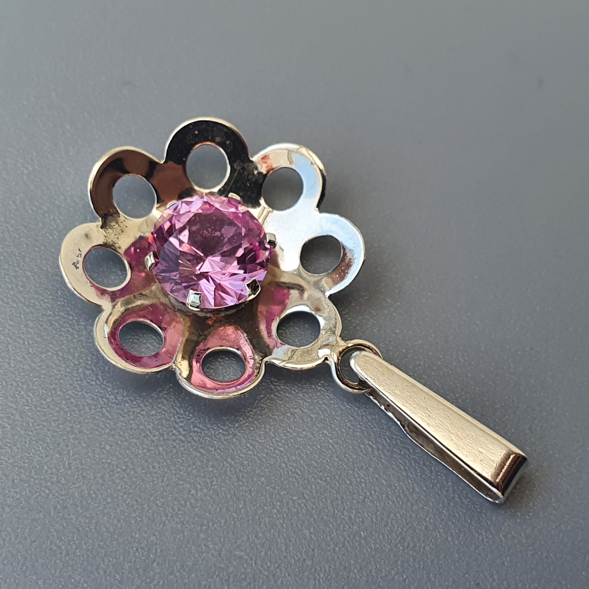 Flower-shaped pendant with a pink gemstone center and circular cutouts in the petals.