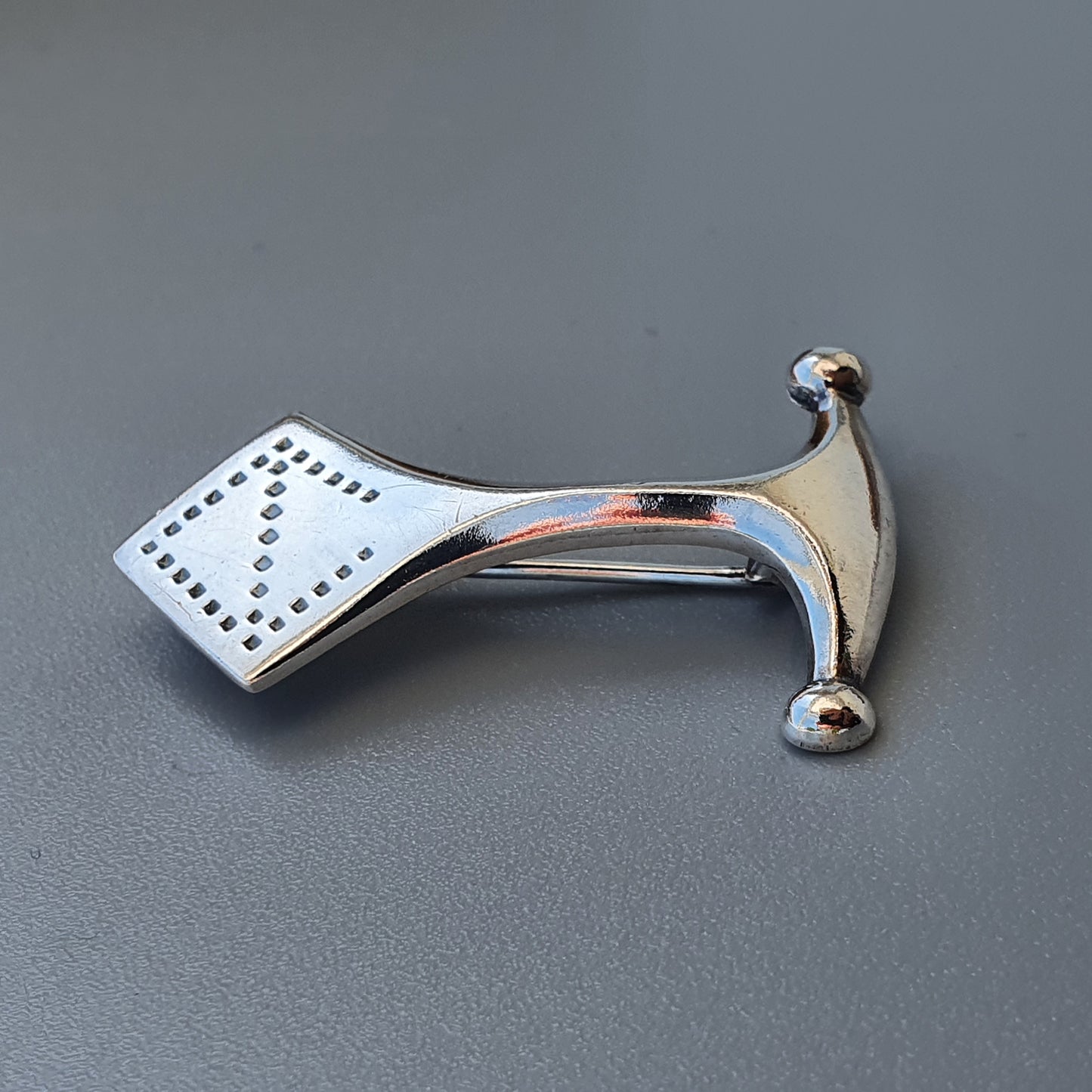 Shiny metallic hammer with a studded rectangular head and curved handle.