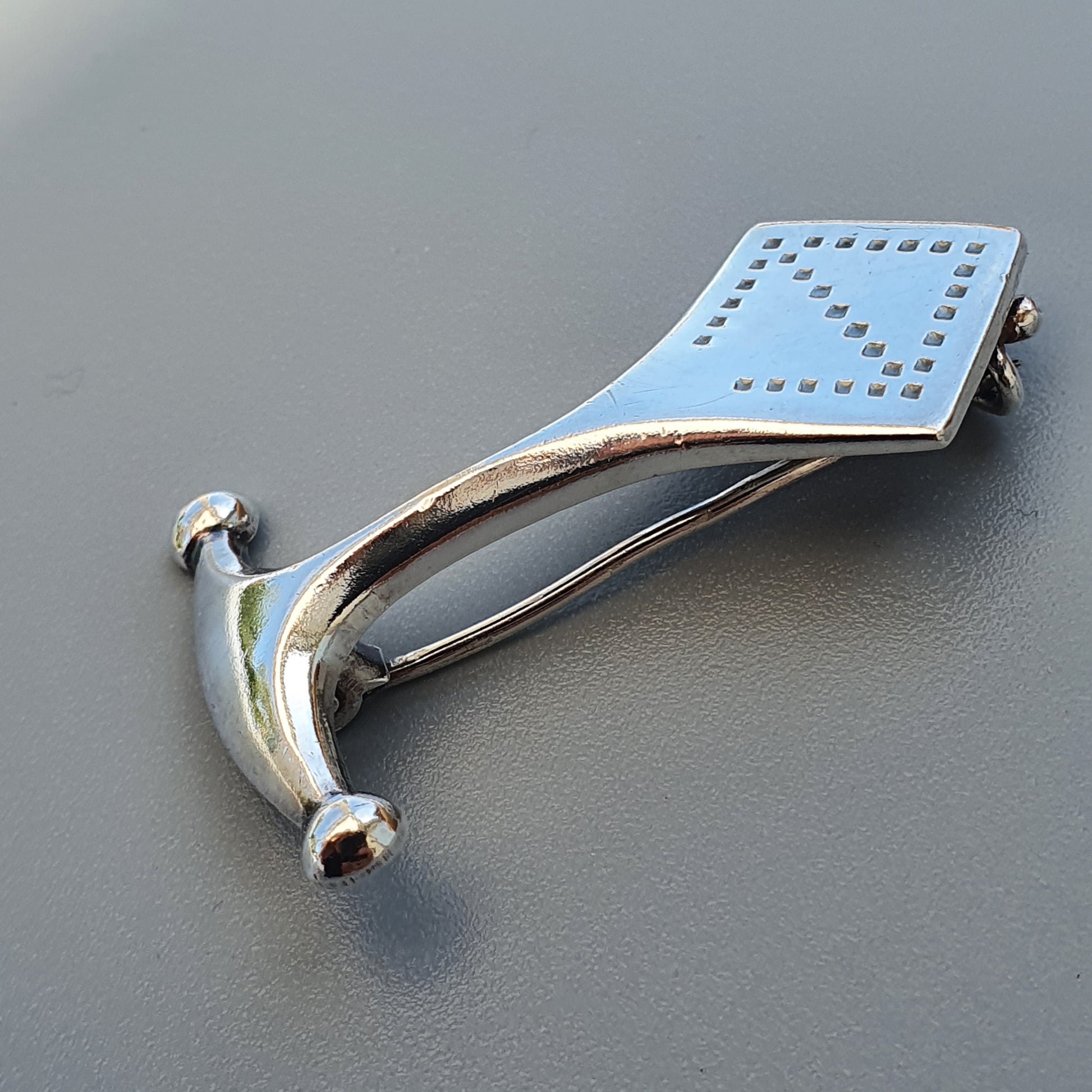 Stylized silver hammer with a square, perforated head and curved handle.