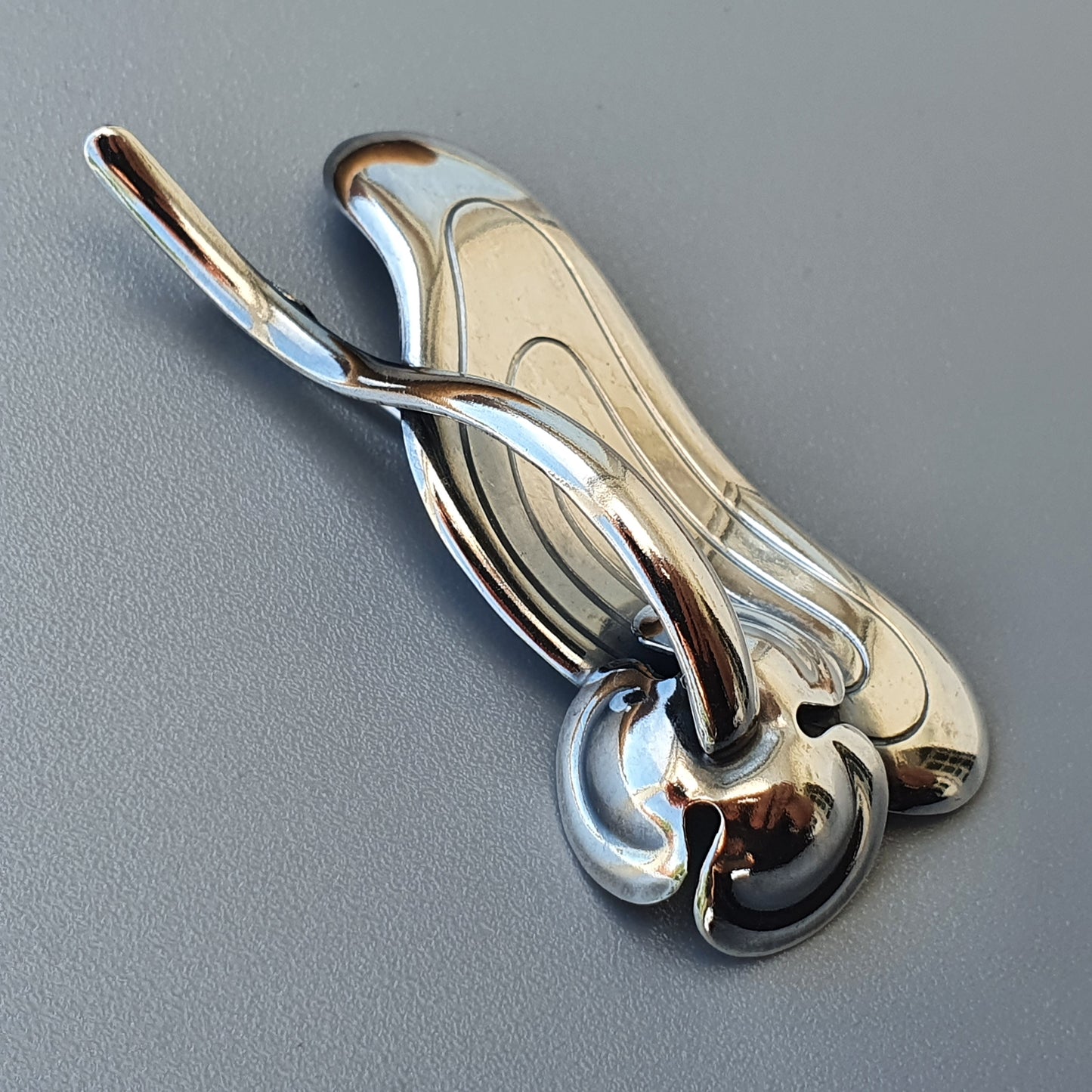 Chrome-plated car hood ornament with a stylized wing or flame design.