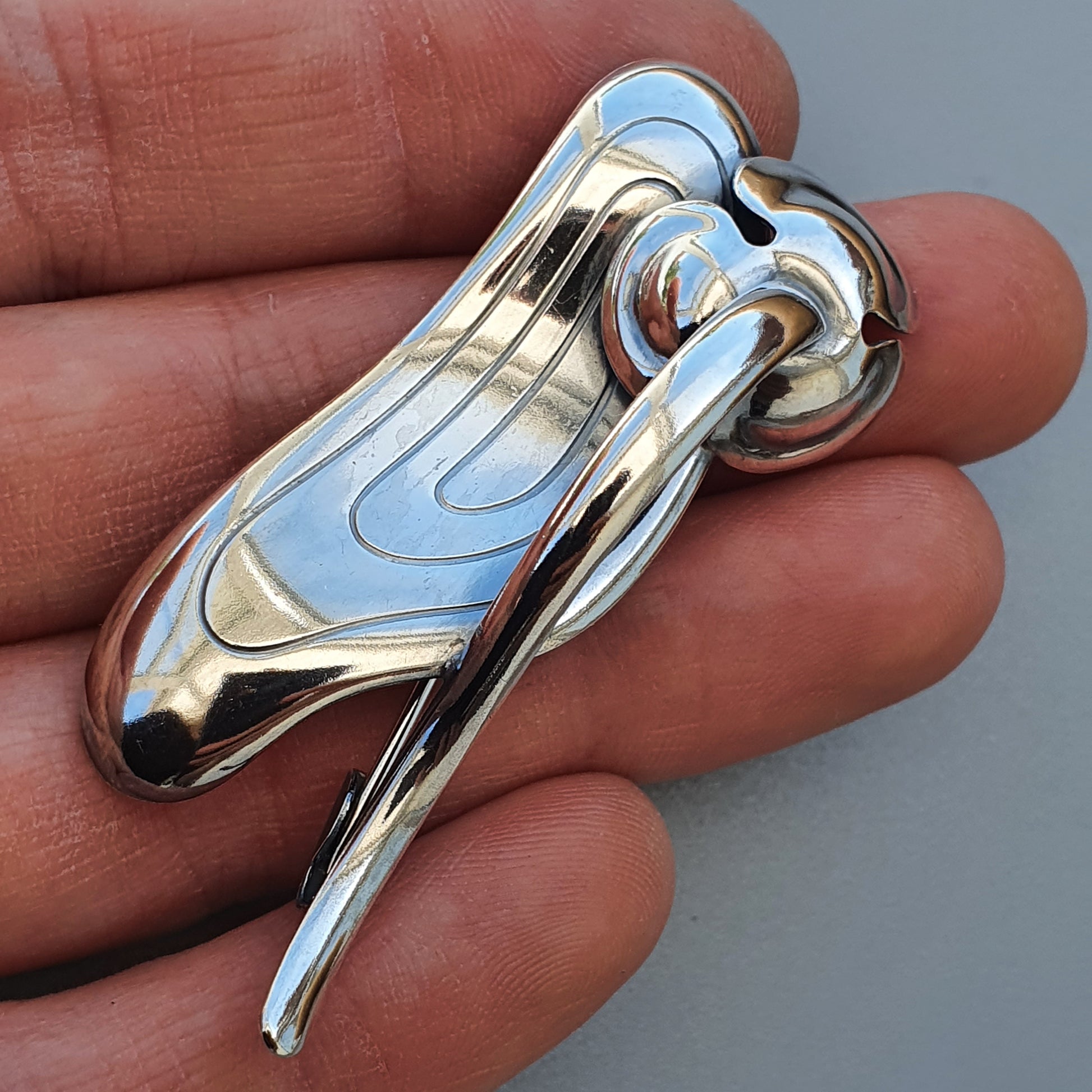 Shiny metallic pendant or charm with a curved, abstract design resembling a stylized figure.