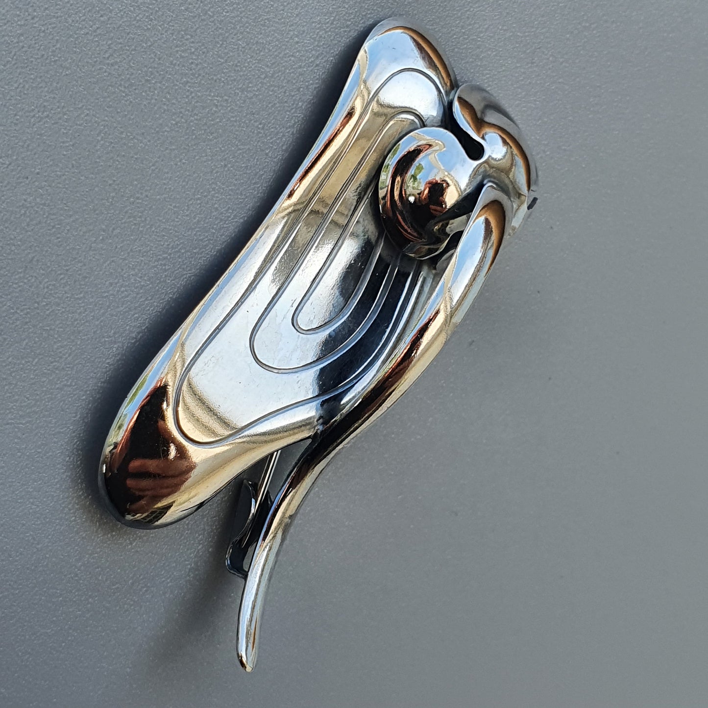 Shiny, chrome door knocker with a curved, abstract design resembling a stylized bird or wing shape.