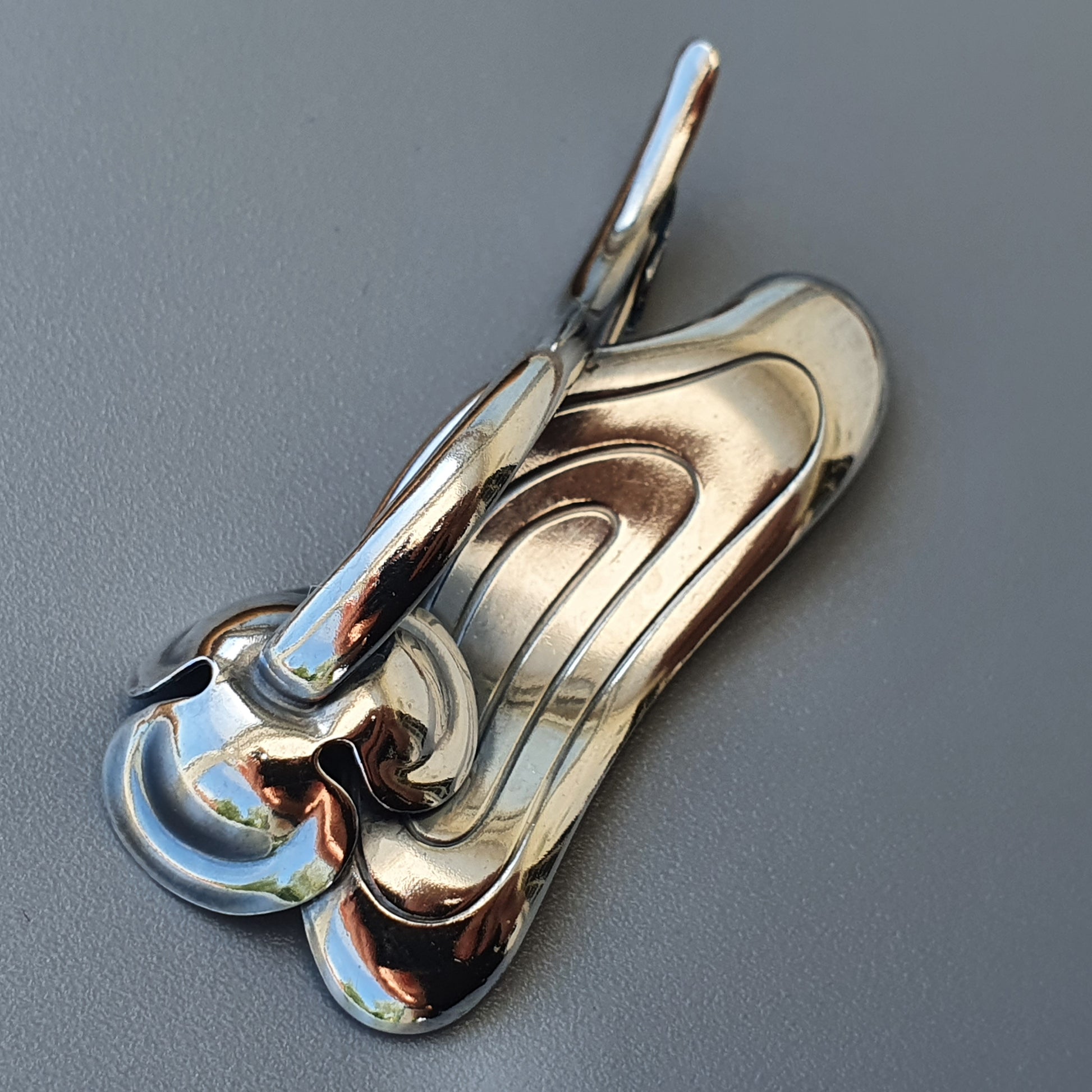 Shiny metallic abstract sculpture with fluid, curved shapes resembling melted or flowing metal.