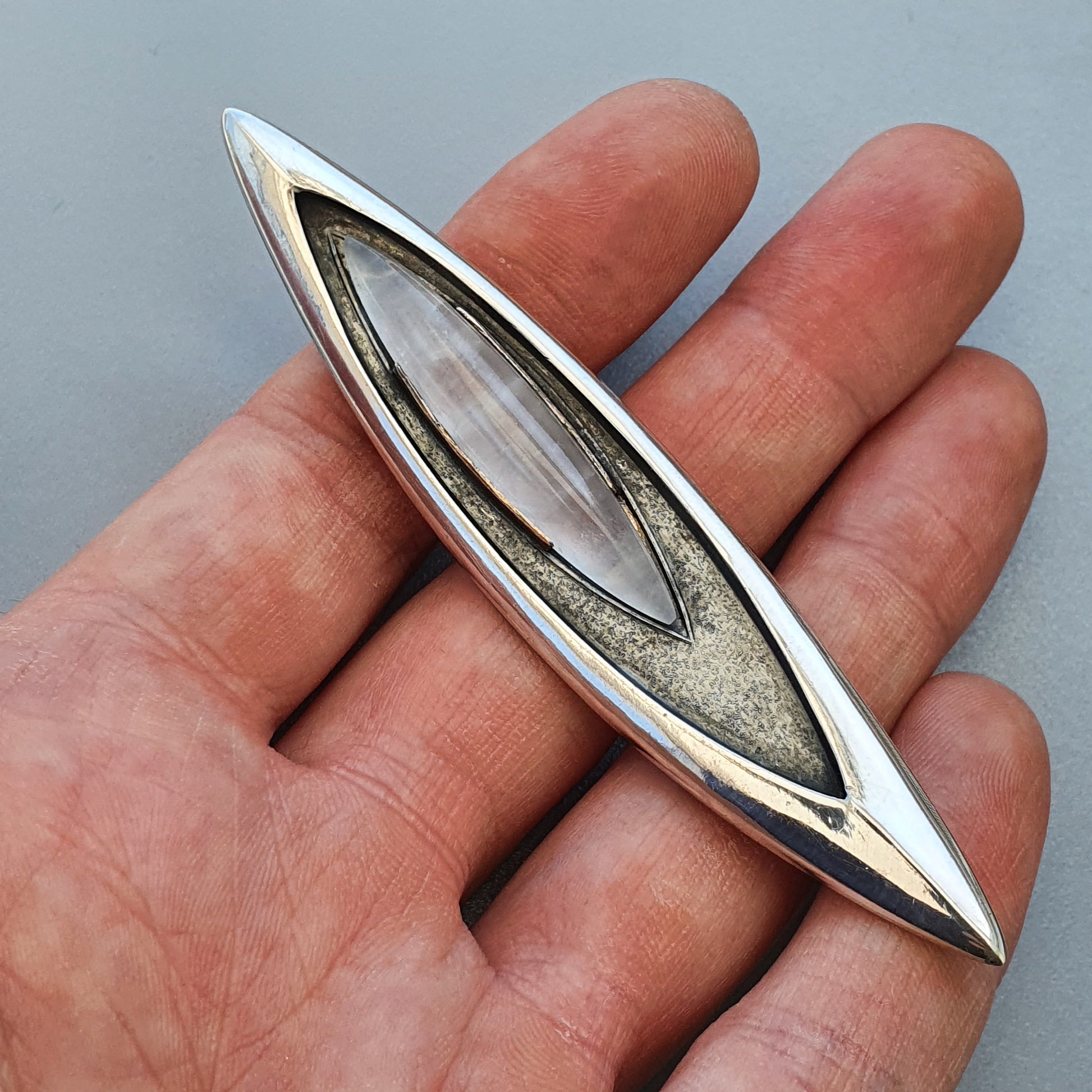 Elongated silver pendant or brooch with a pointed oval shape and inlaid center.