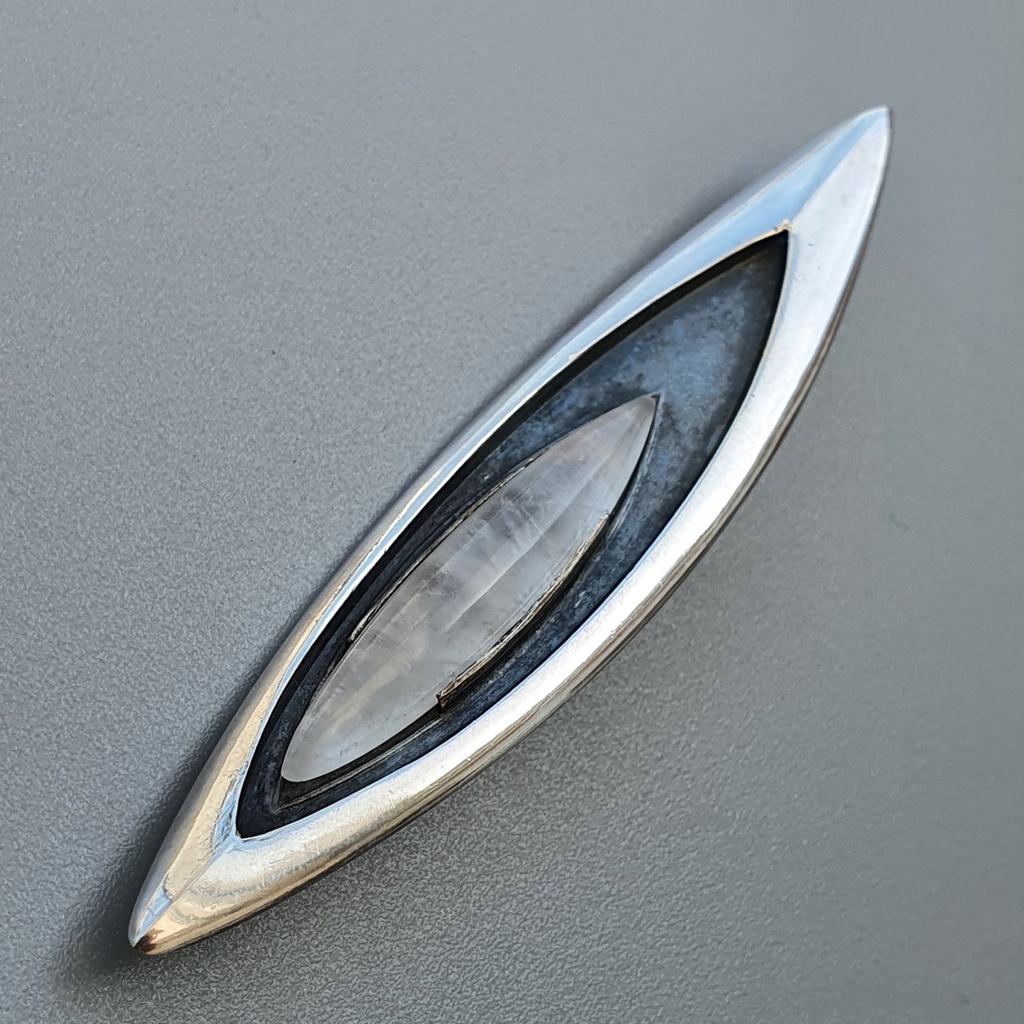 Sleek, eye-shaped car emblem or logo with metallic silver edges and a dark center.