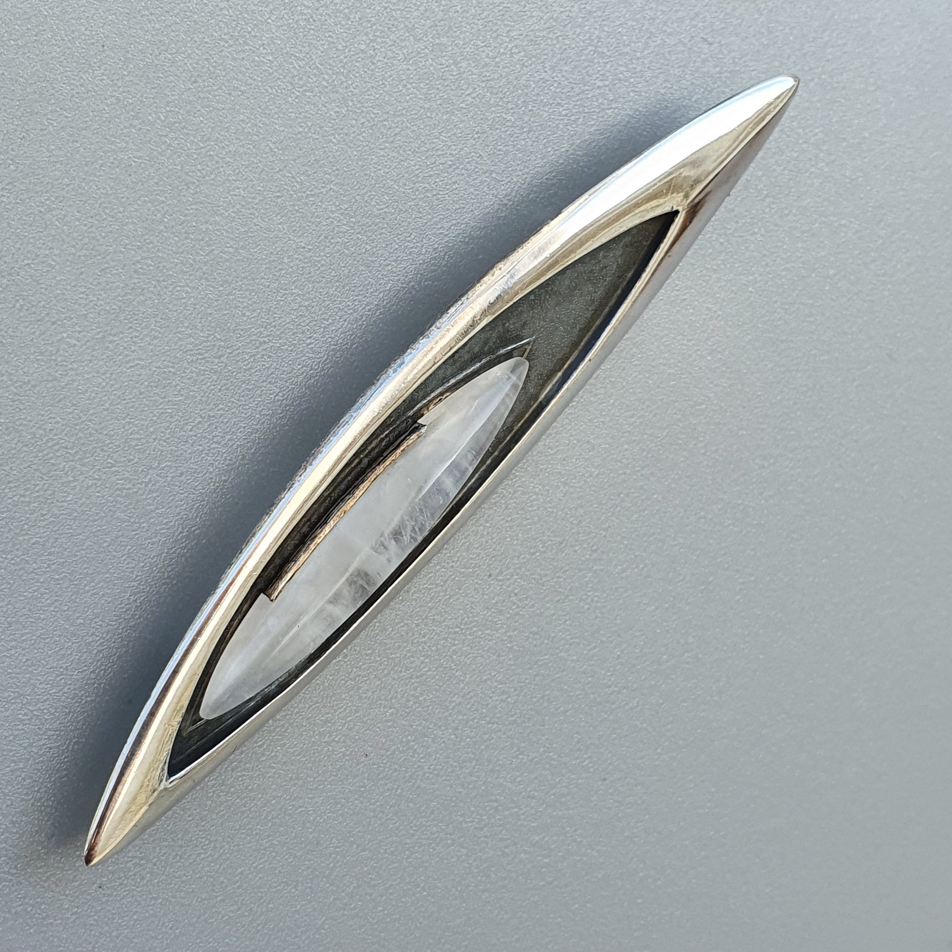 Sleek, elongated silver brooch with an eye-shaped opening containing a pearl-like center.