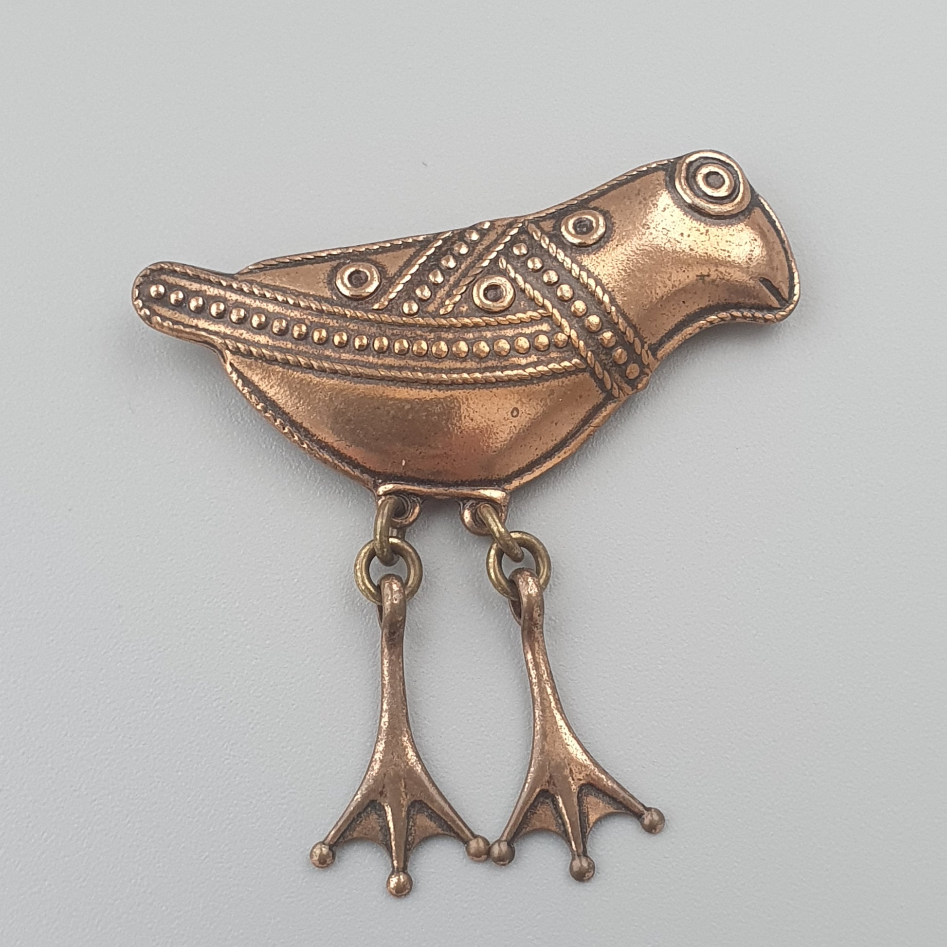 Bronze or copper ornament shaped like a stylized bird with decorative patterns and dangling feet.