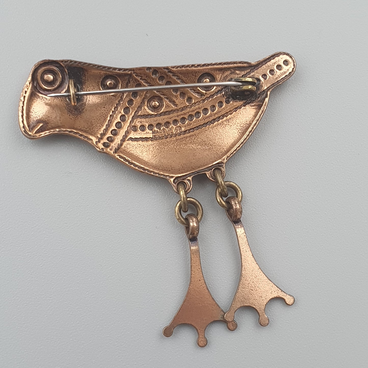 Stylized copper or bronze bird-shaped brooch with dangling feet charms.