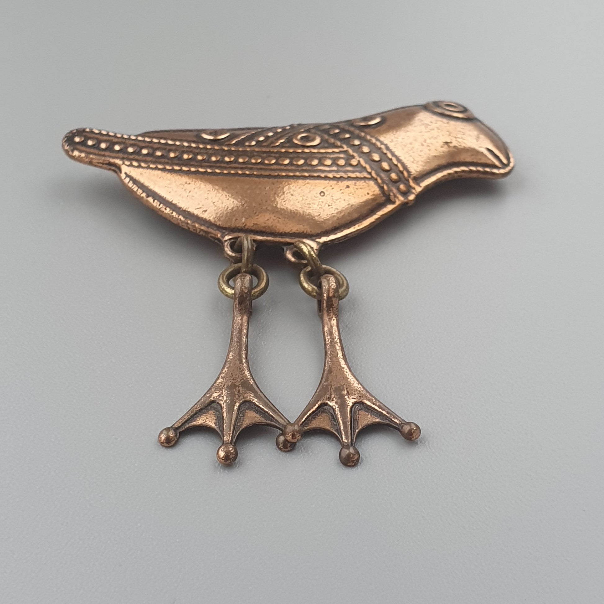 Copper-colored bird-shaped brooch with decorative feet.