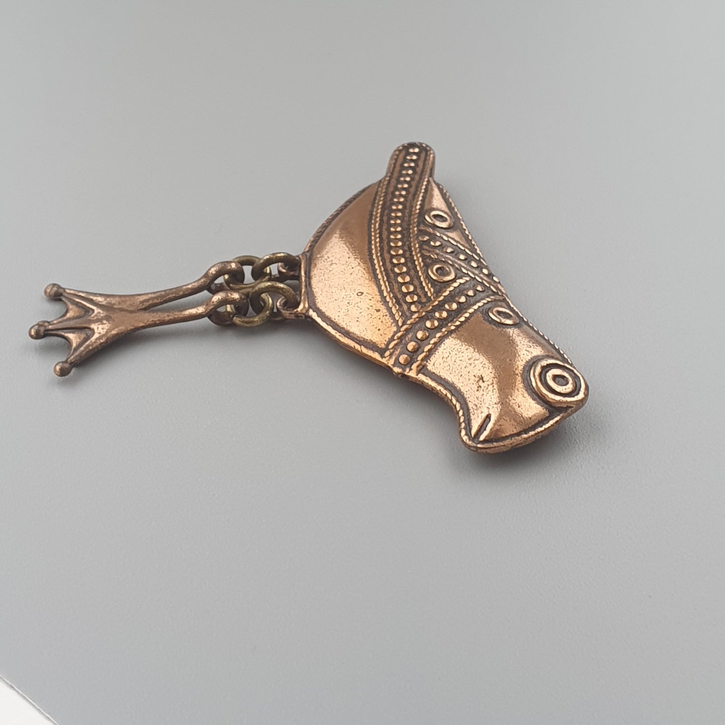 Bronze or copper-colored decorative fish-shaped pendant or charm with intricate patterns.