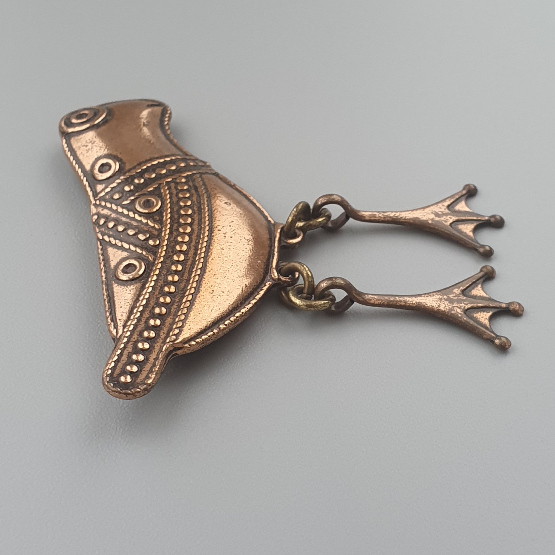 Ornate copper or bronze bird-shaped pendant with intricate patterns and two branching feet.