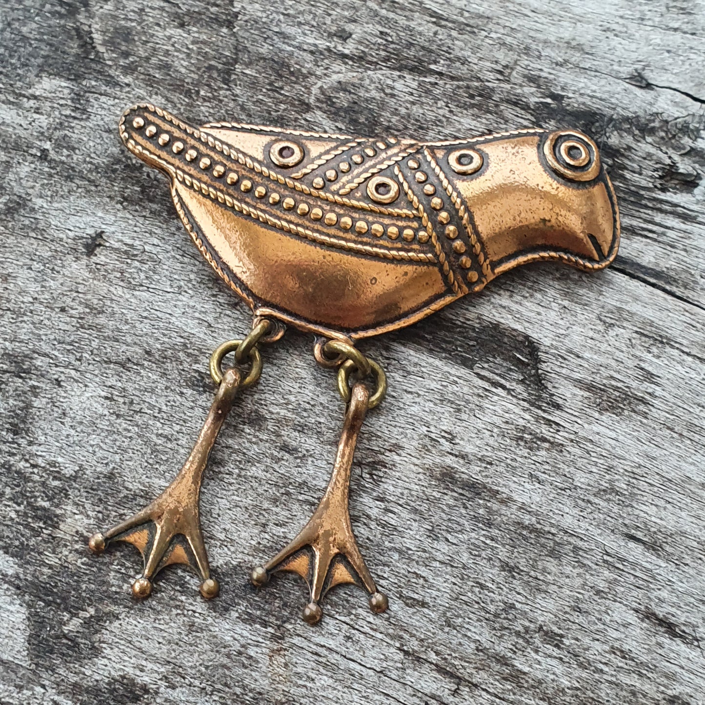 Decorative bronze bird-shaped brooch with intricate patterns and dangling feet.