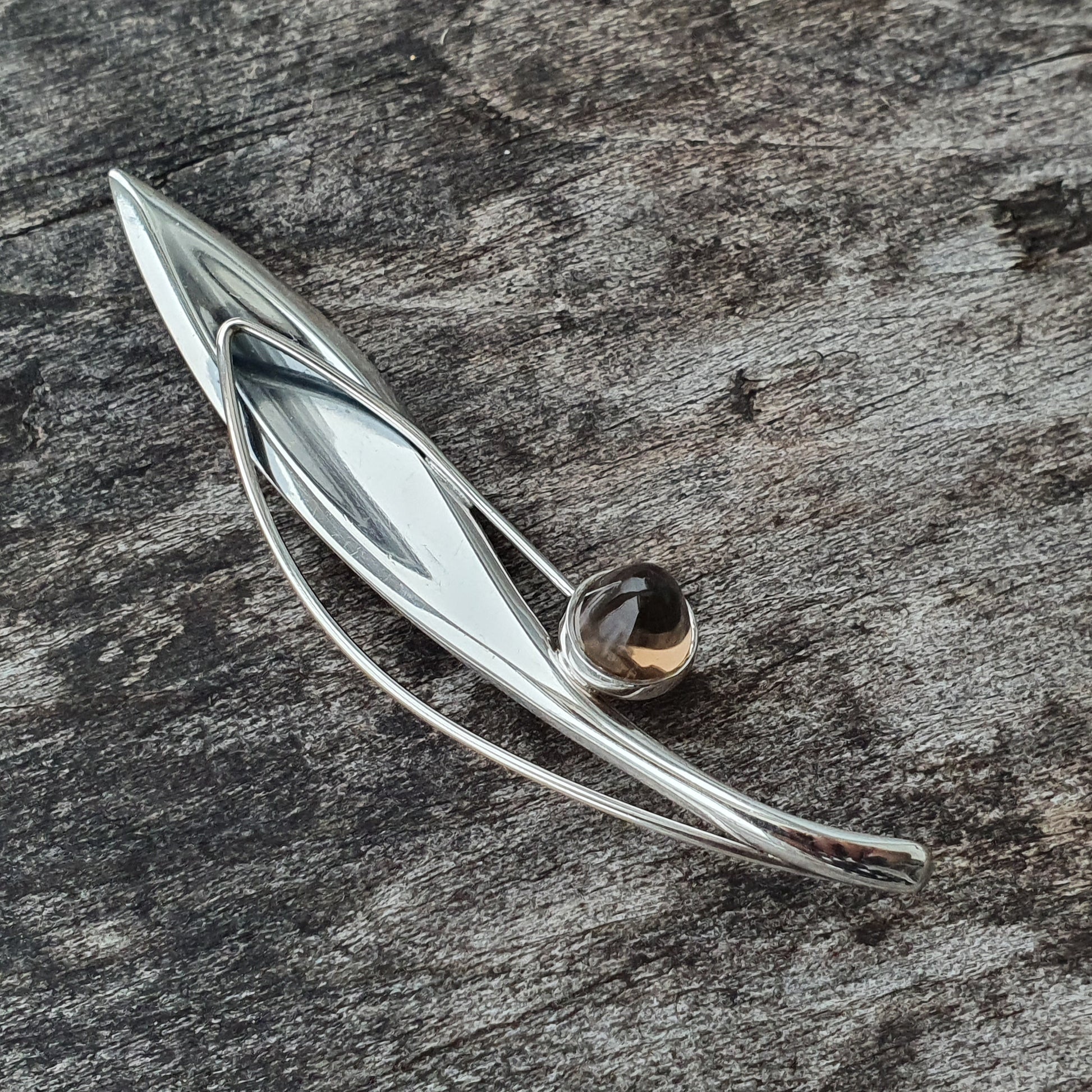 Silver feather-shaped brooch or pin with a small gemstone accent.