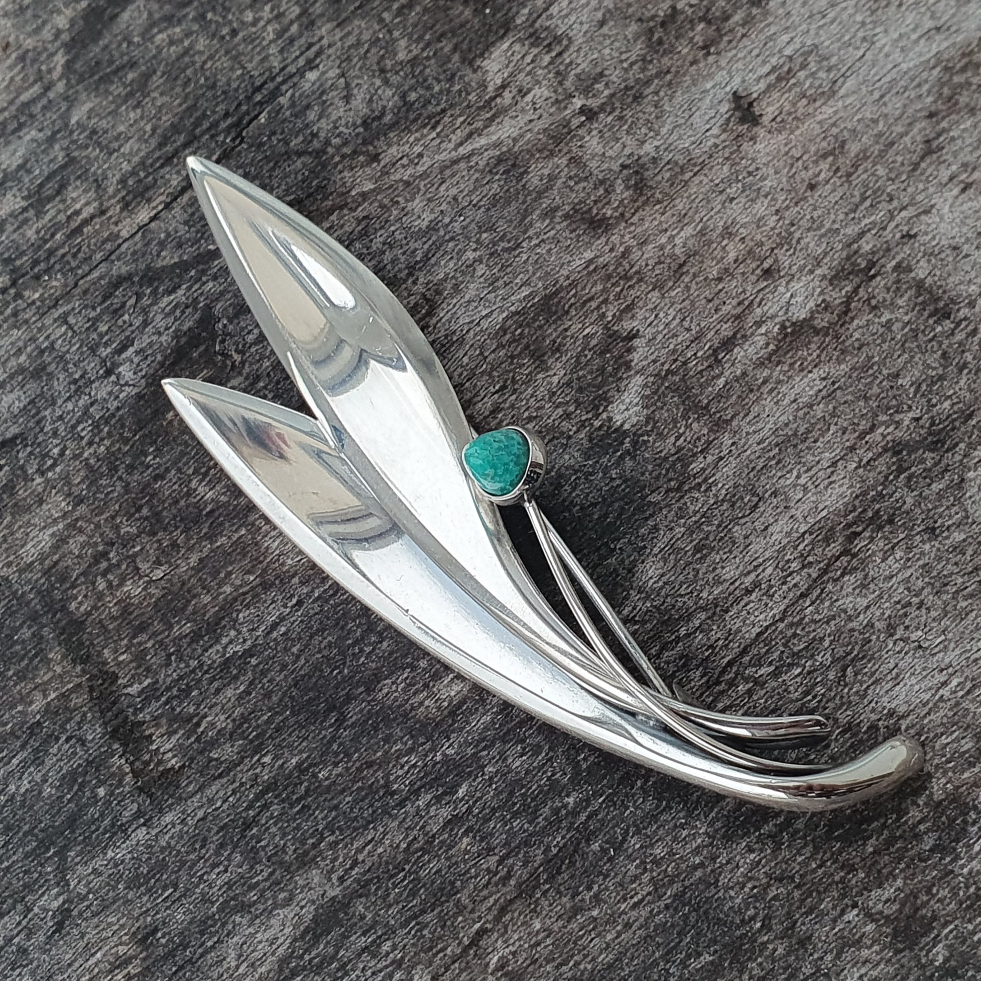 Silver brooch or pin shaped like stylized leaves with a small turquoise stone accent.