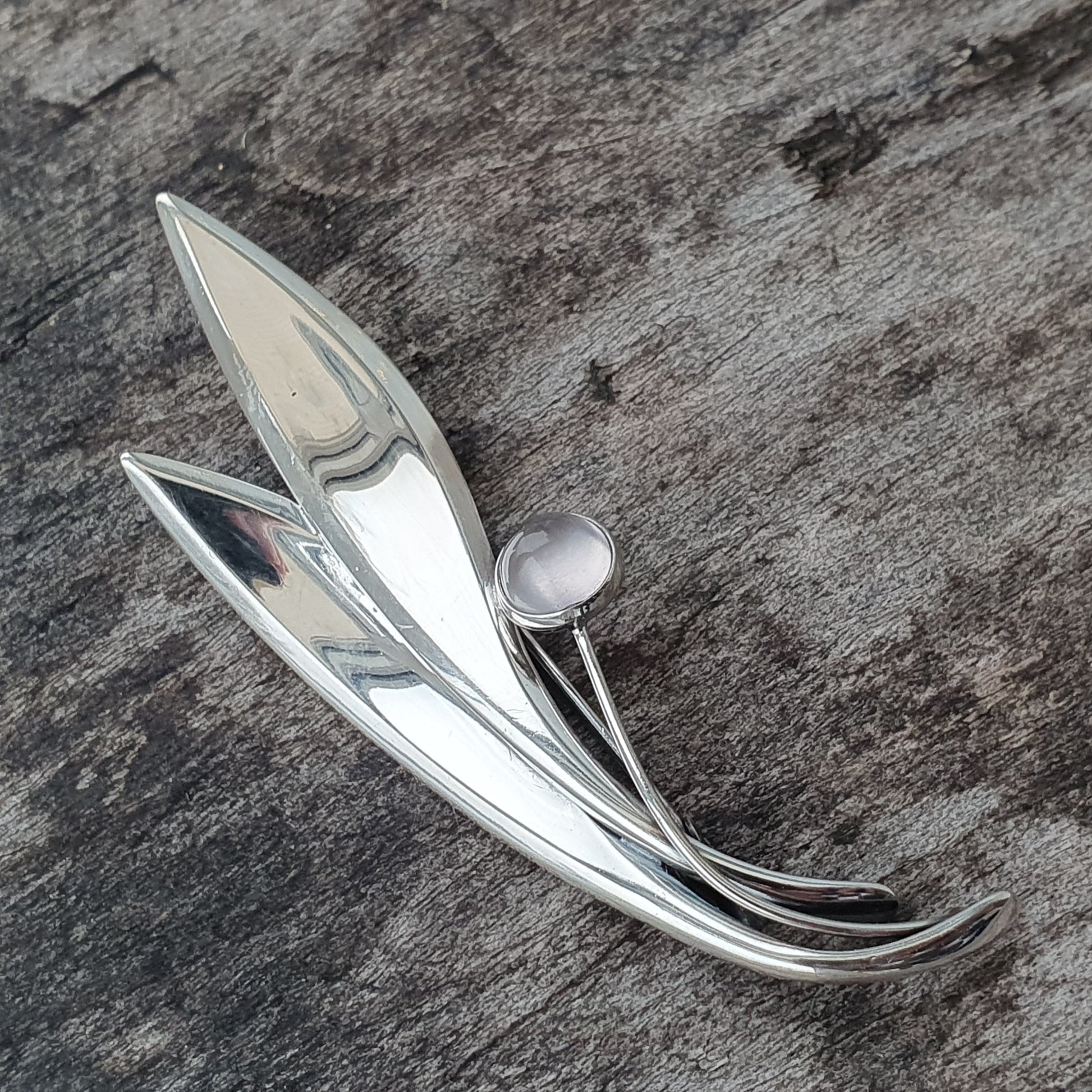 Silver brooch shaped like a stylized flower or leaf with a pearl accent.