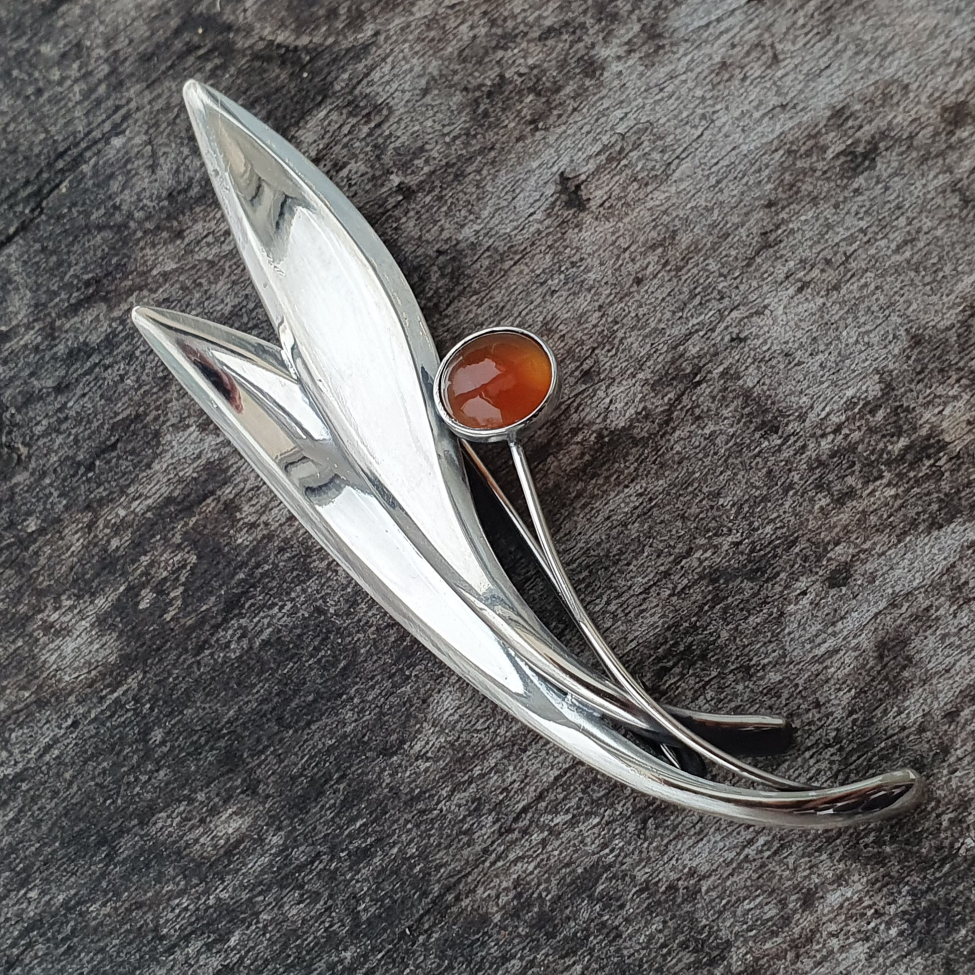 Silver brooch with leaf-like design and amber-colored stone accent.