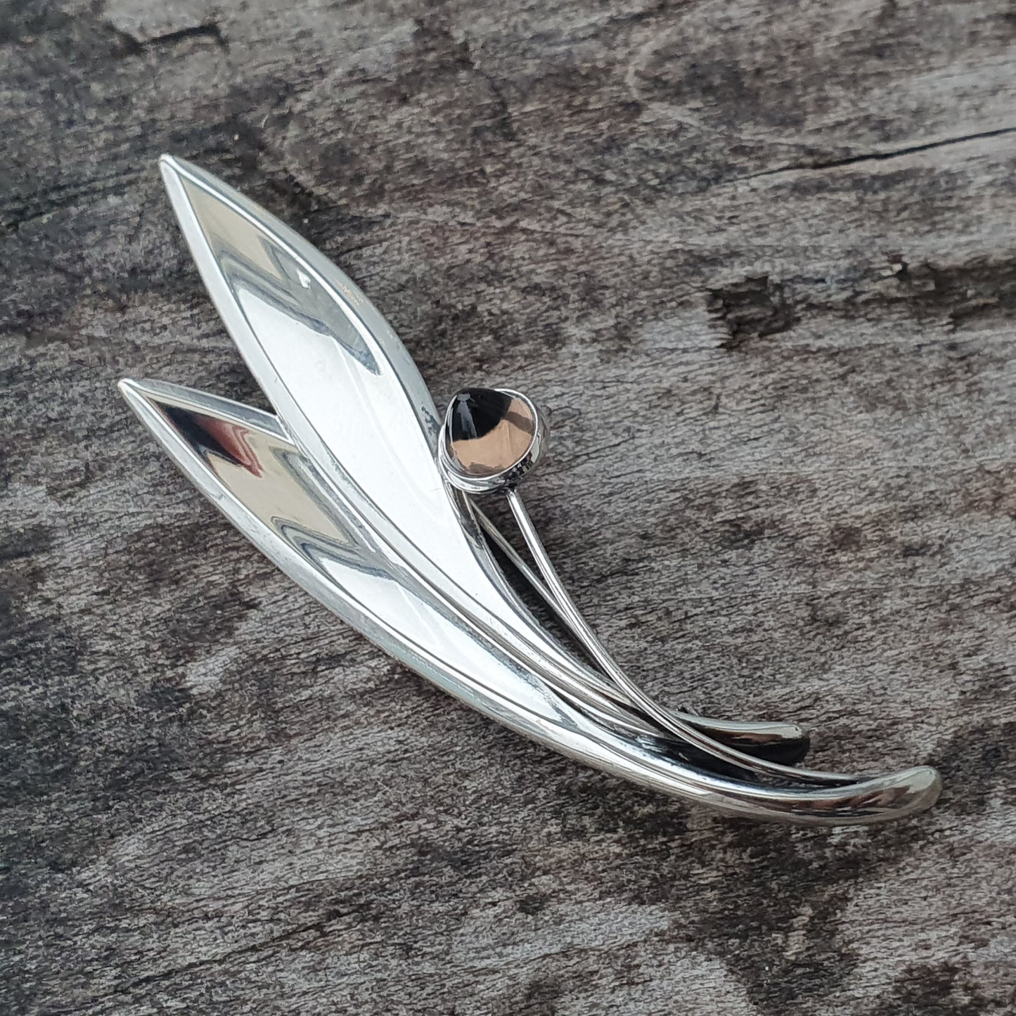 Silver brooch shaped like stylized leaves or feathers with a small gemstone accent.