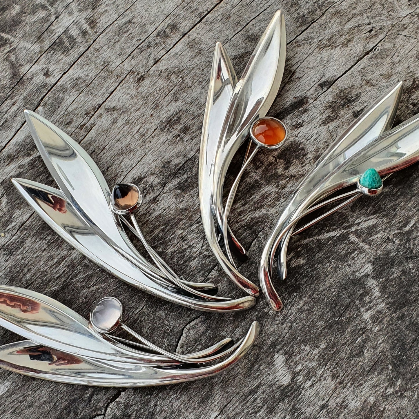 Silver leaf-shaped brooches adorned with colorful gemstones.