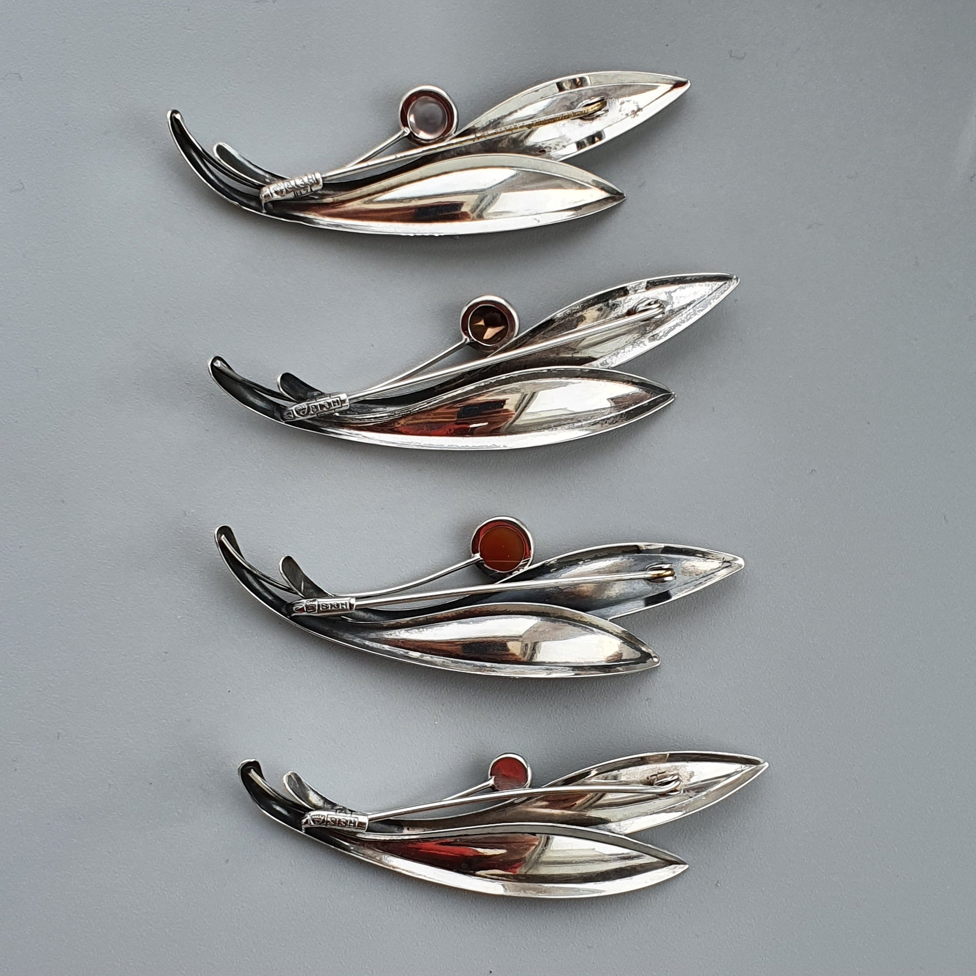 Sleek, leaf-shaped silver brooches or pins with colored gemstone accents.