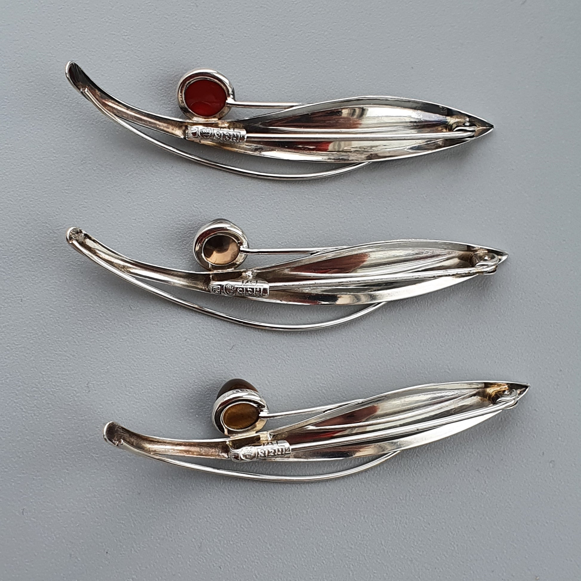 Silver brooches or pins shaped like stylized leaves with gemstone accents.