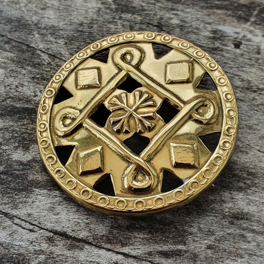 Ornate gold-colored circular brooch or medallion with geometric and floral designs.