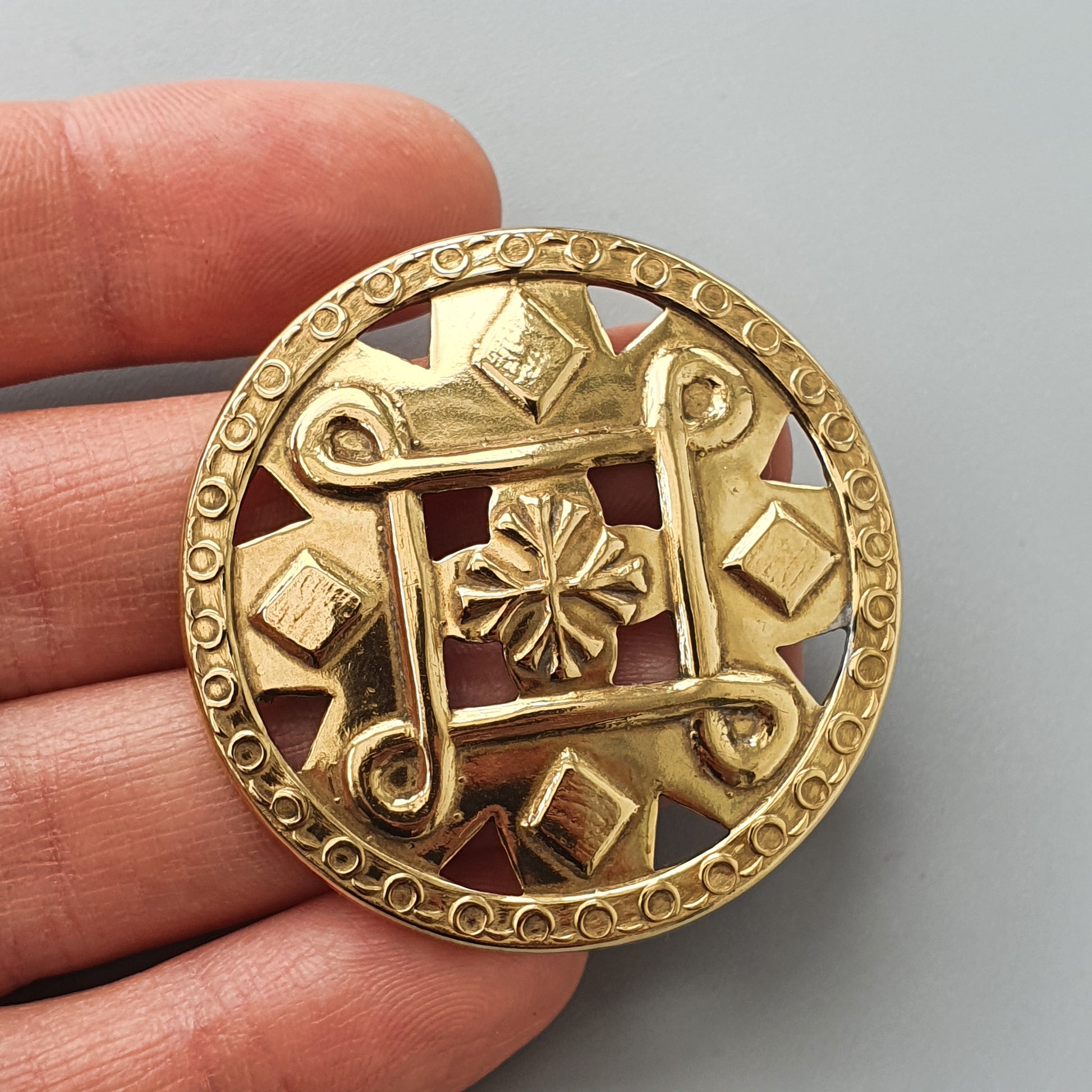 Ornate gold-colored circular brooch with geometric and floral designs.