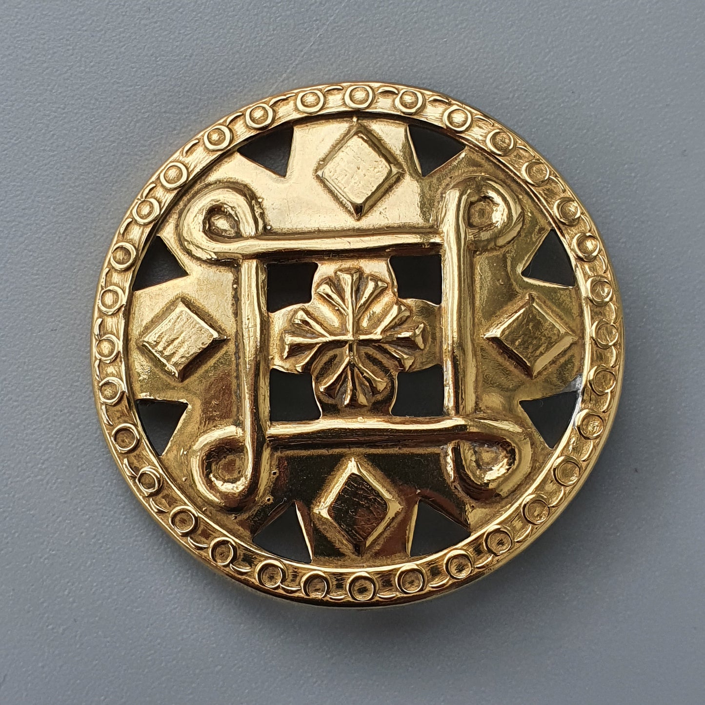 Ornate circular gold brooch or medallion with intricate geometric and floral designs.