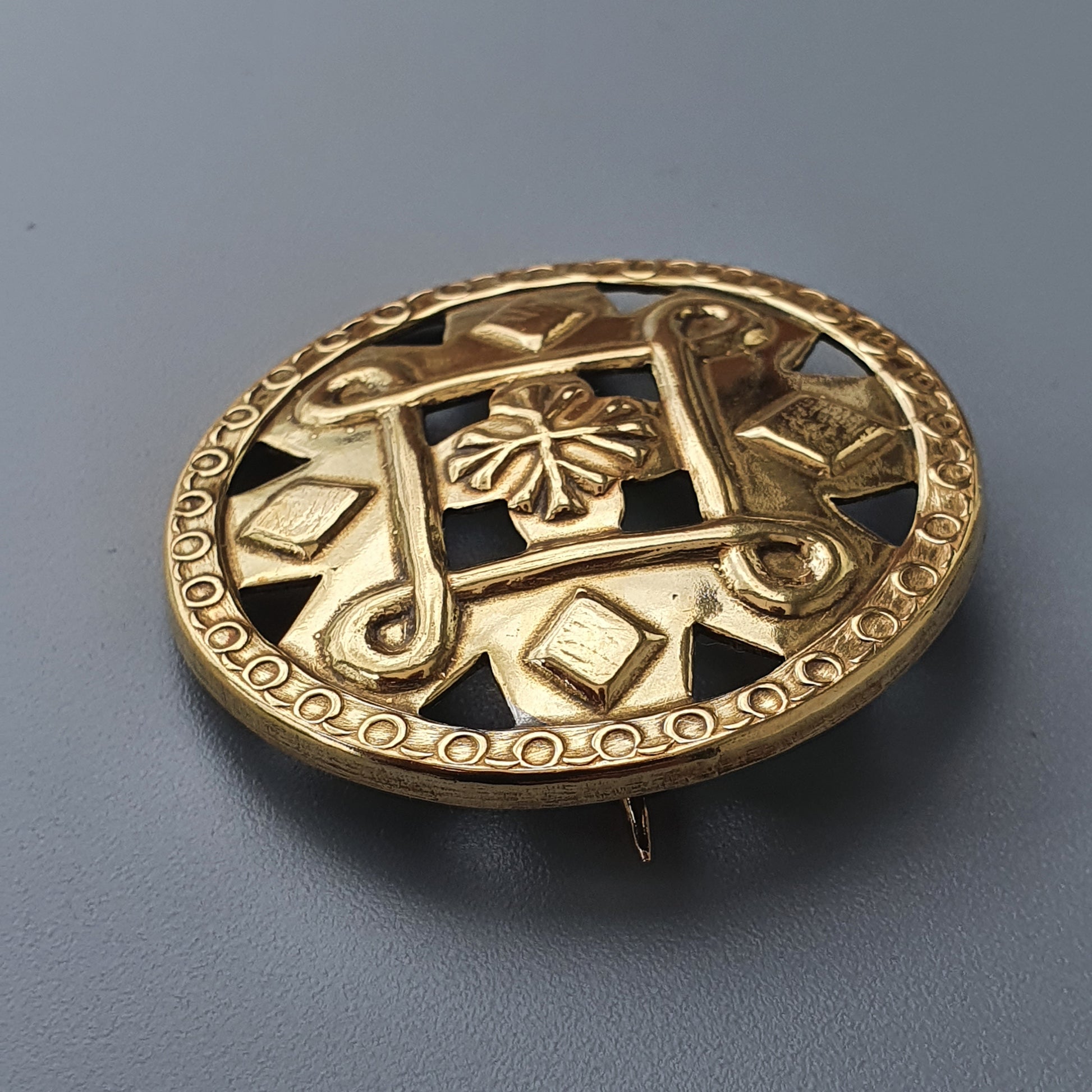 Ornate gold brooch with intricate designs including a clover or flower motif.