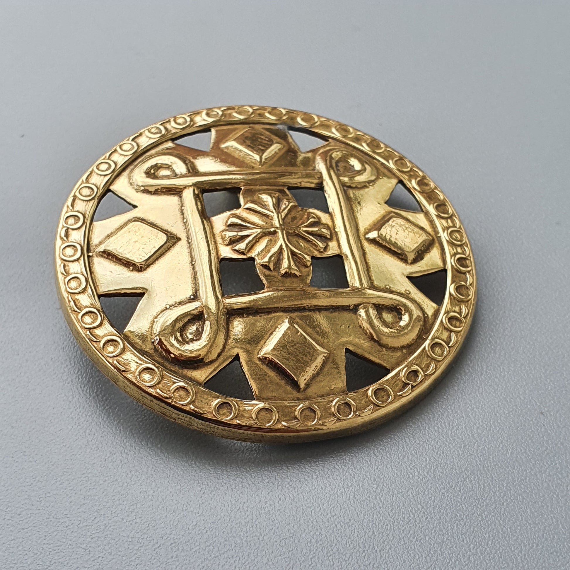 Gold-colored ornate circular brooch or medallion with floral and geometric designs.