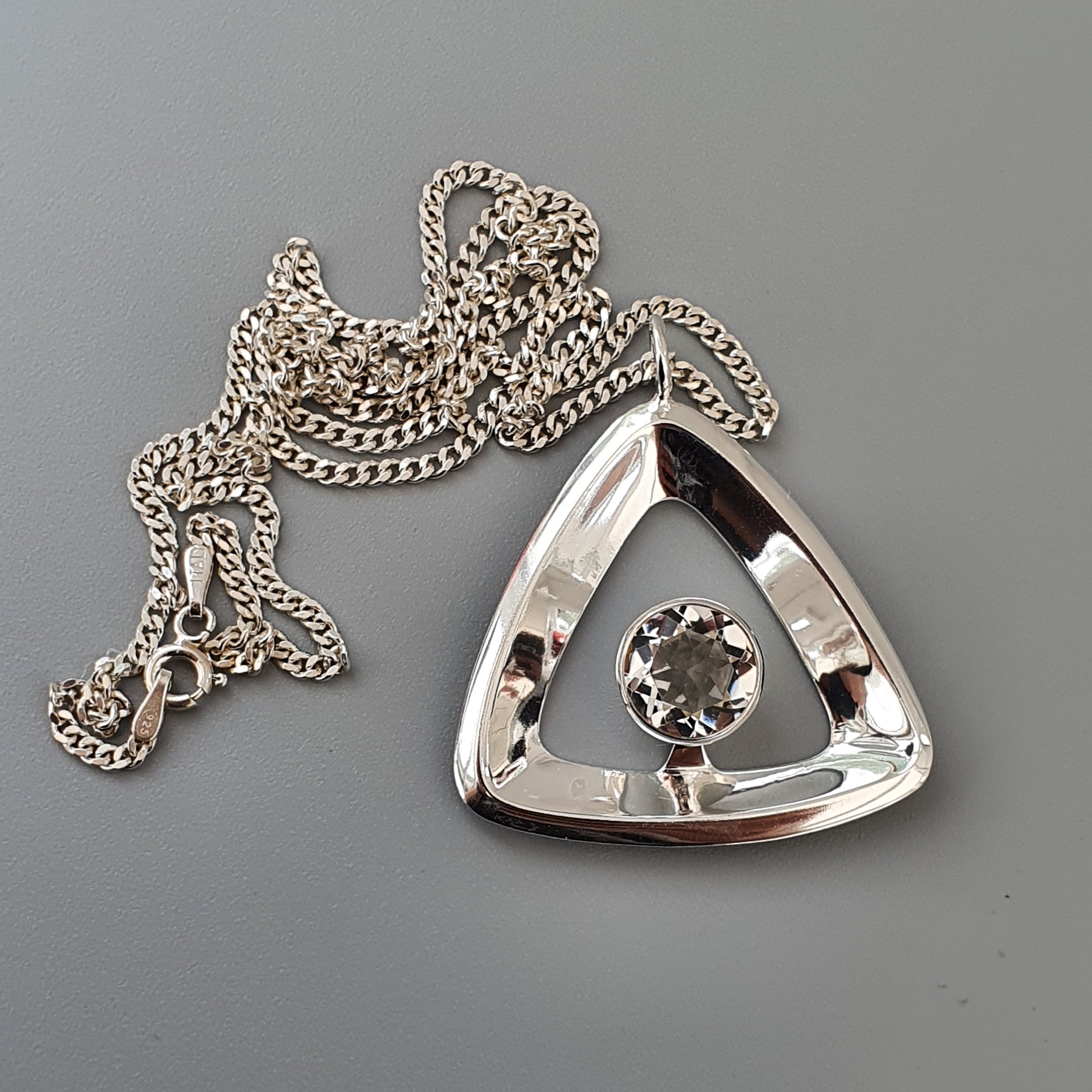 Triangular silver pendant with a central gemstone, attached to a chain necklace.