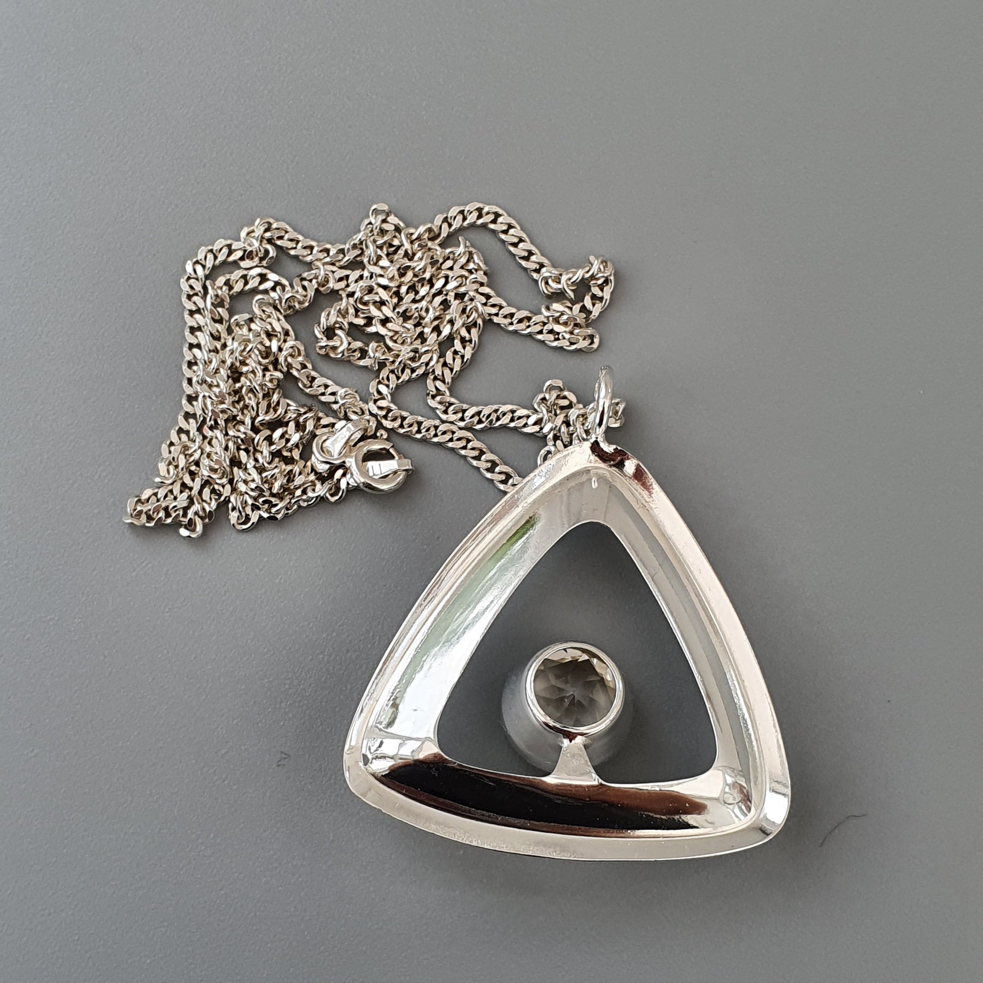 Silver triangular pendant necklace with a spherical gemstone in the center.