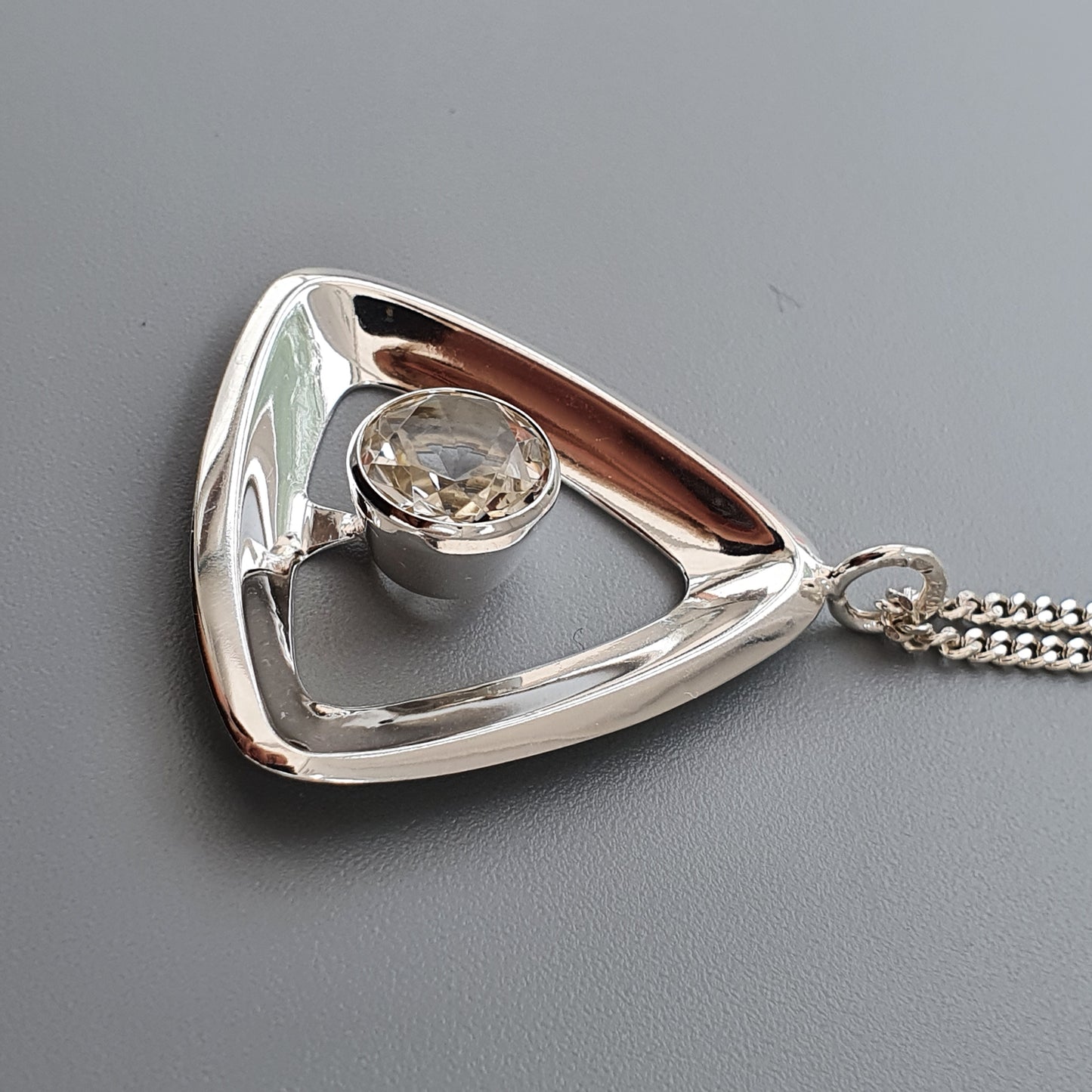 Triangular silver pendant with a round gemstone set in the center, attached to a chain.