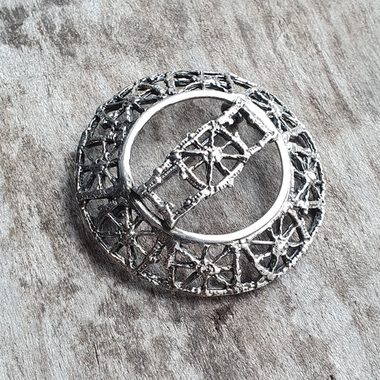 Circular silver brooch with intricate geometric filigree design.