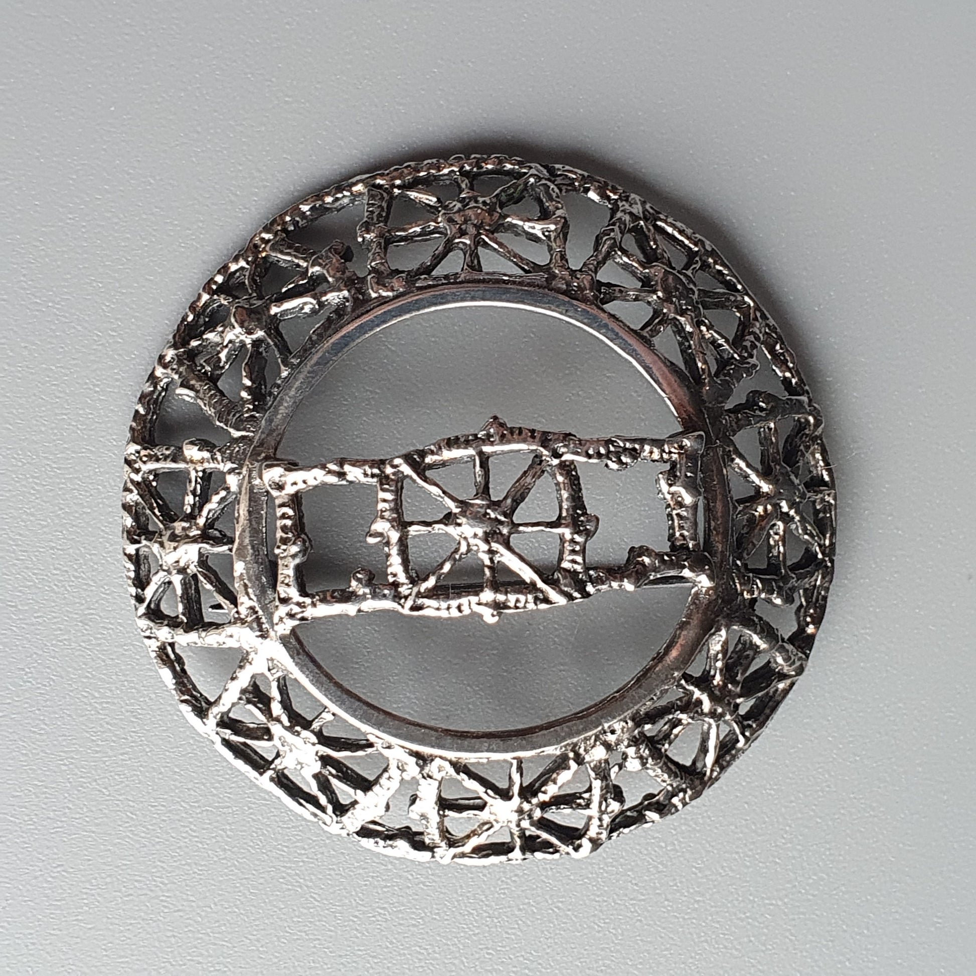 Circular silver brooch with intricate geometric cutout patterns.