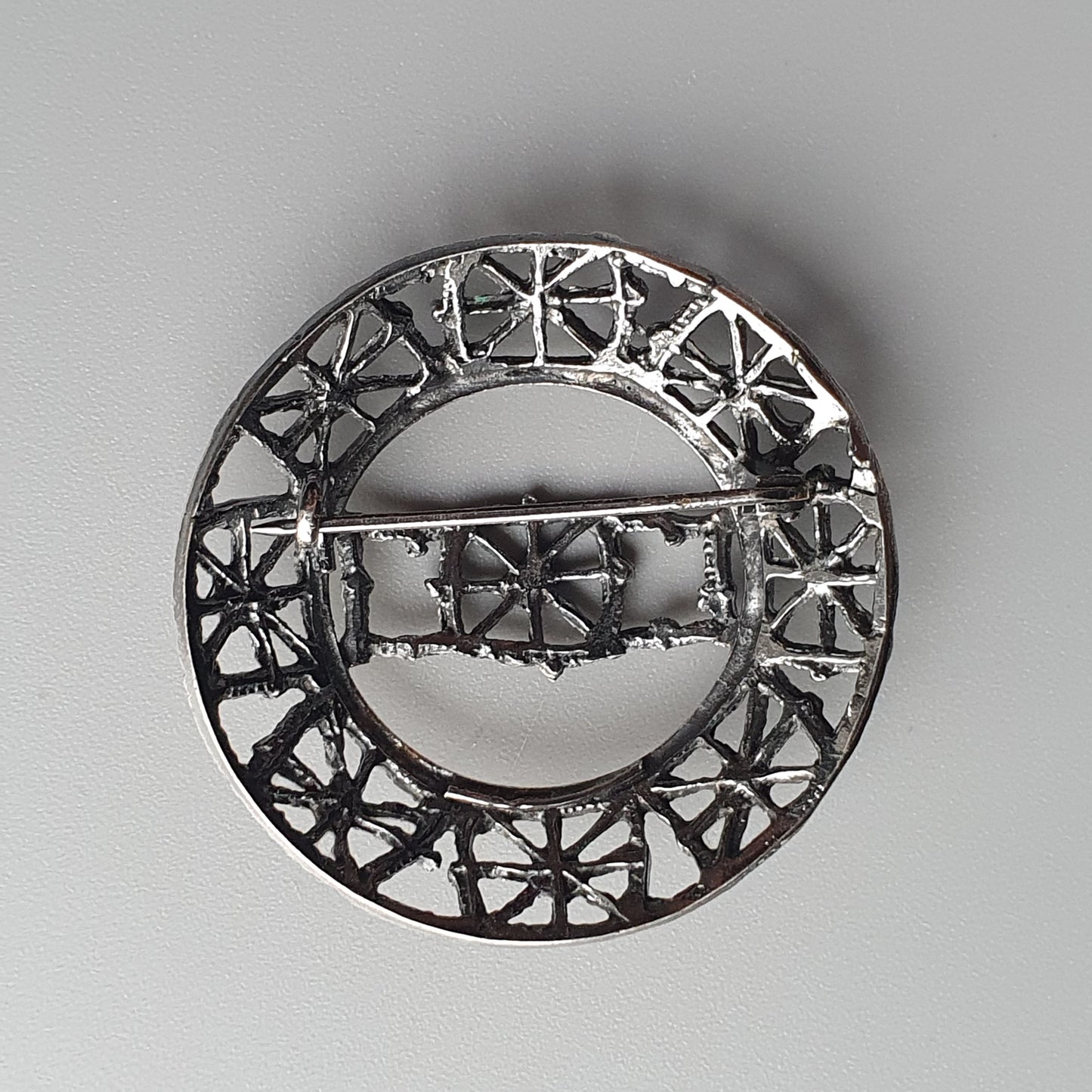 Circular silver brooch with intricate geometric cutout design.