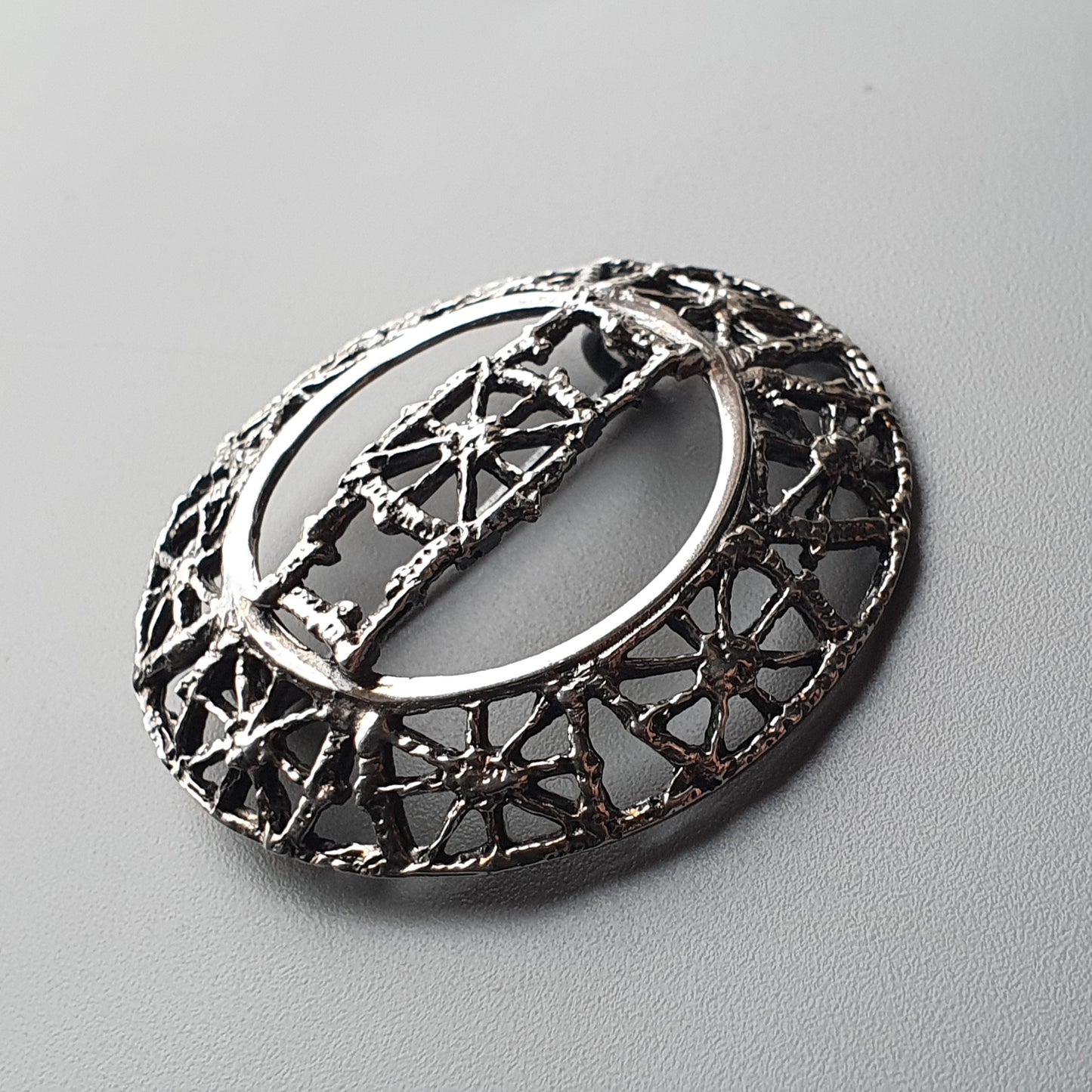 Ornate silver brooch with intricate filigree design in an oval shape.