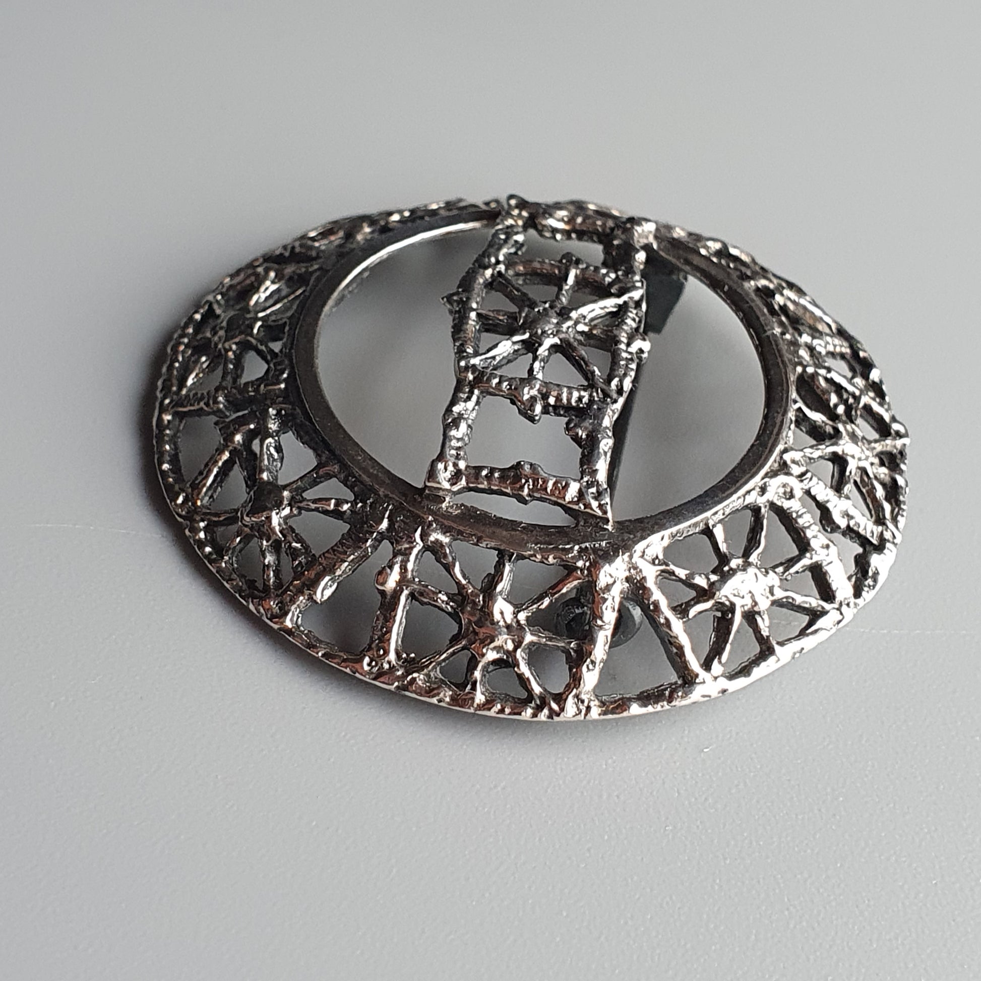 Ornate silver brooch with intricate geometric patterns and an oval shape.