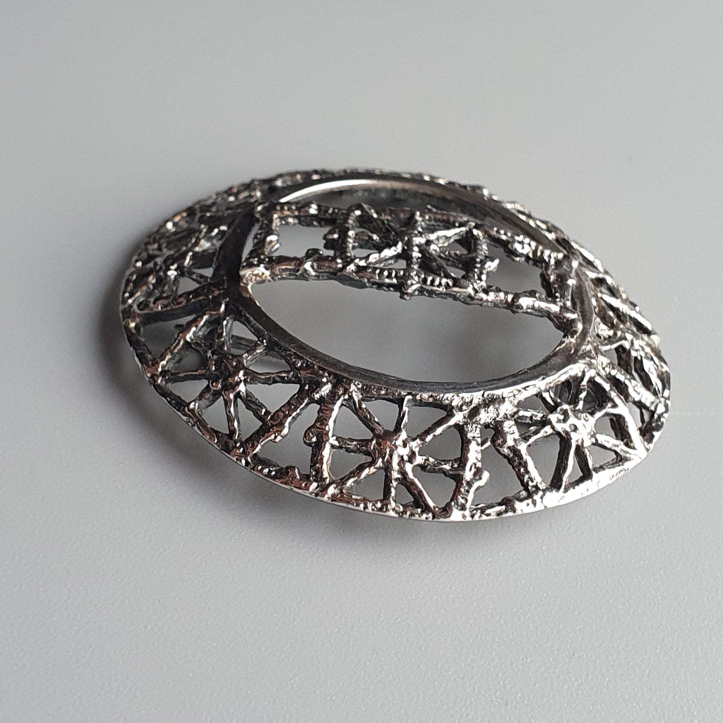 Ornate silver brooch with intricate filigree design and oval shape.