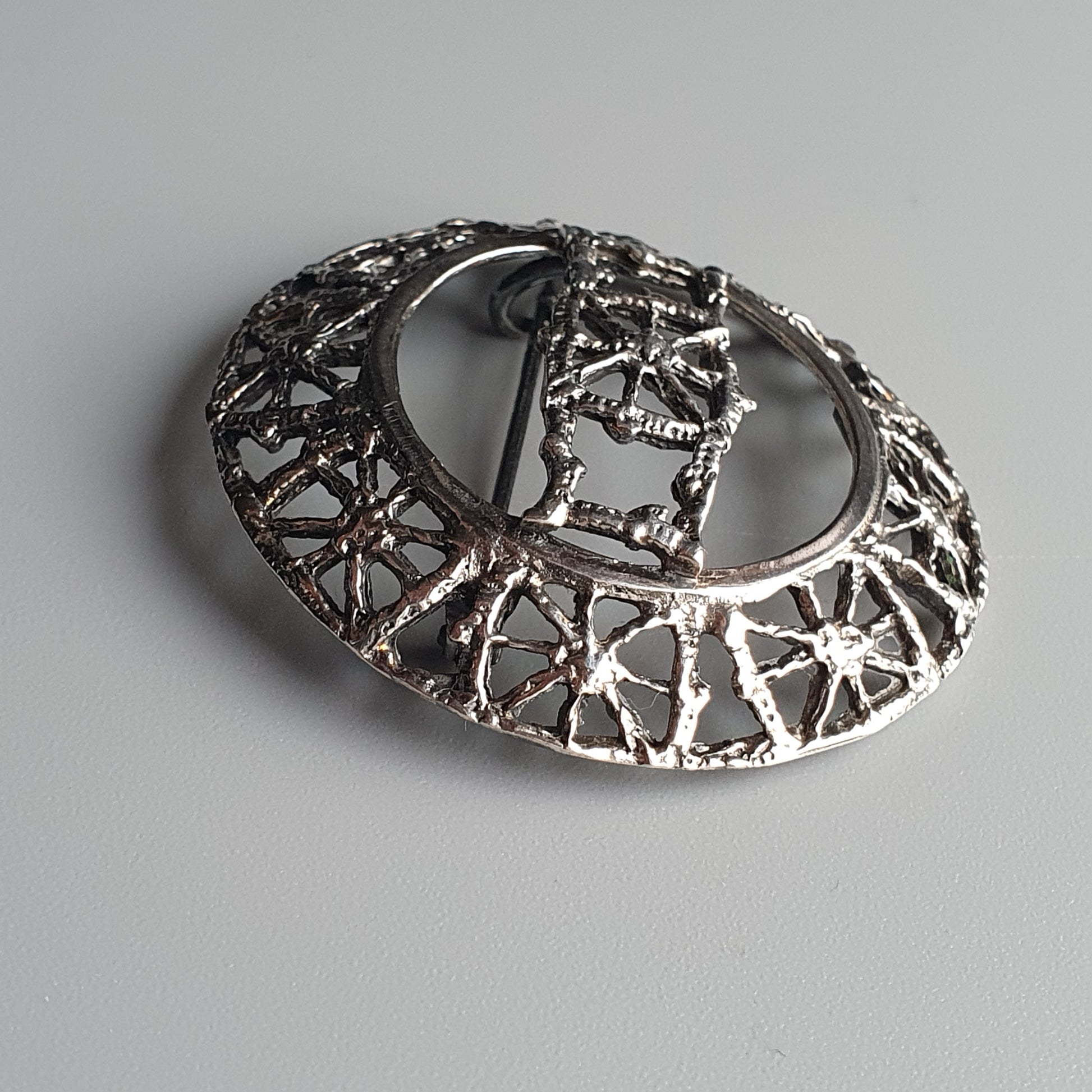 Ornate silver brooch with intricate filigree design and a central decorative element.