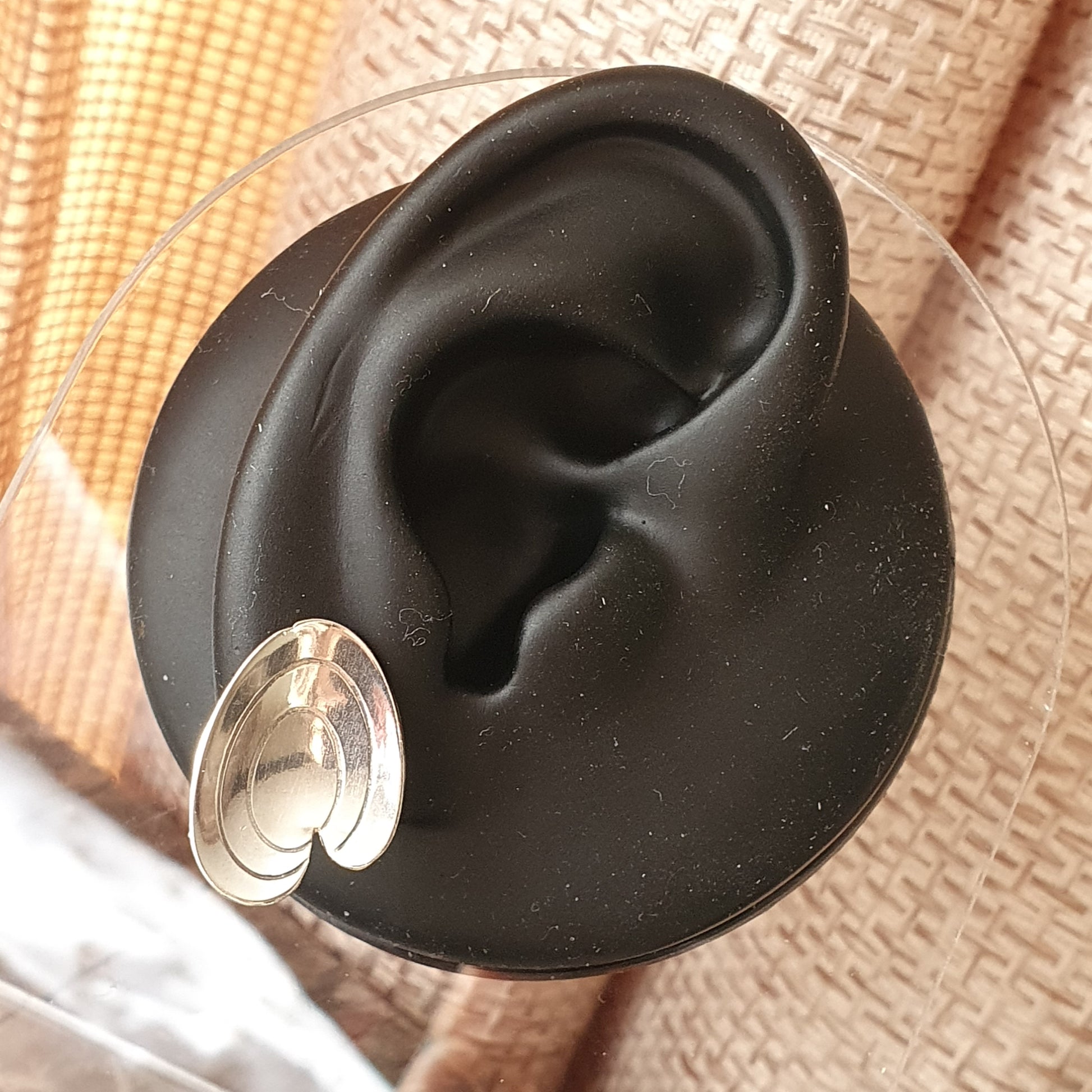 Black plastic model of a human ear with a silver earring inserted in the lobe.