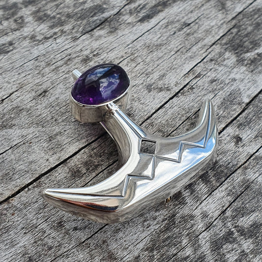 Silver-colored metal pendant or jewelry piece shaped like a crescent moon with a purple gemstone.