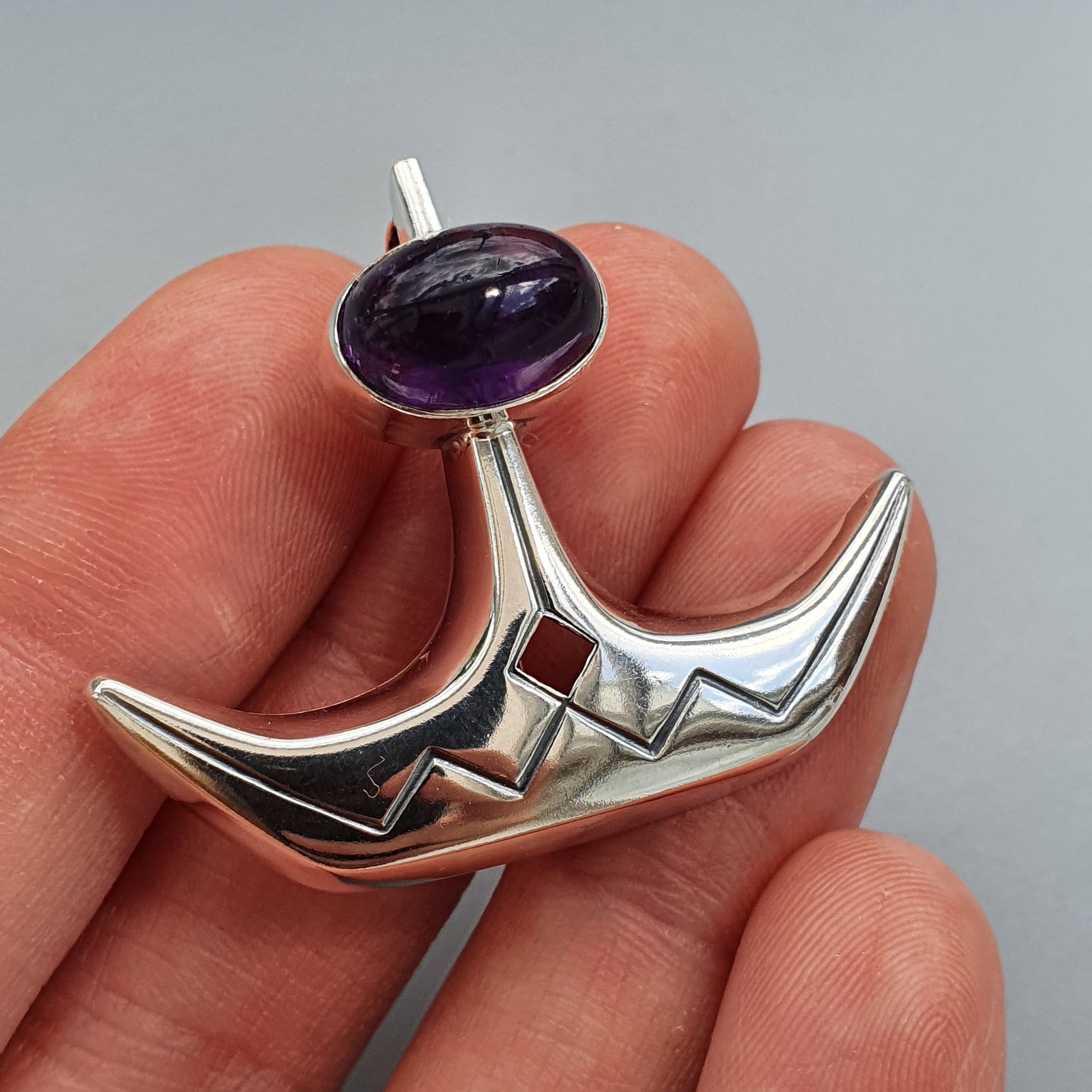 Silver pendant or brooch shaped like a crescent moon with a purple gemstone.