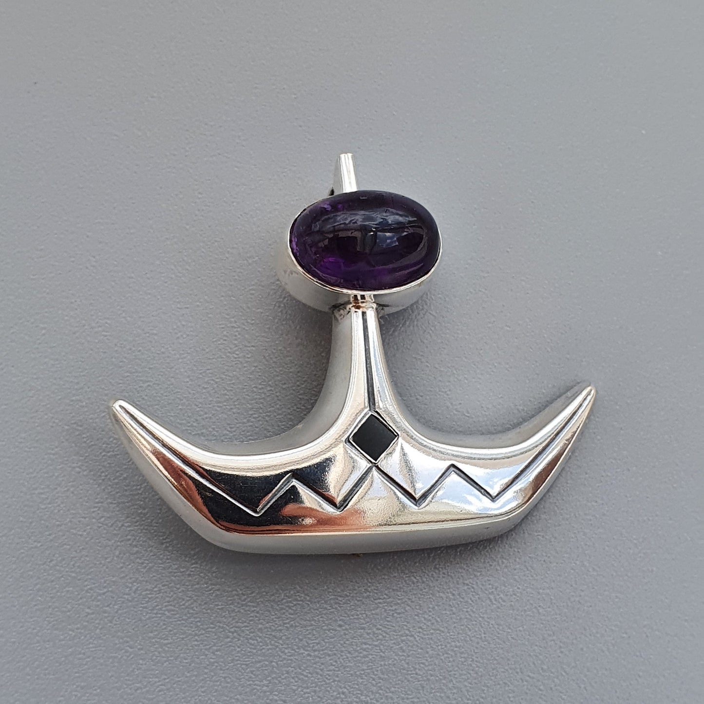 Silver pendant shaped like a stylized boat or crescent with a purple gemstone at the top.