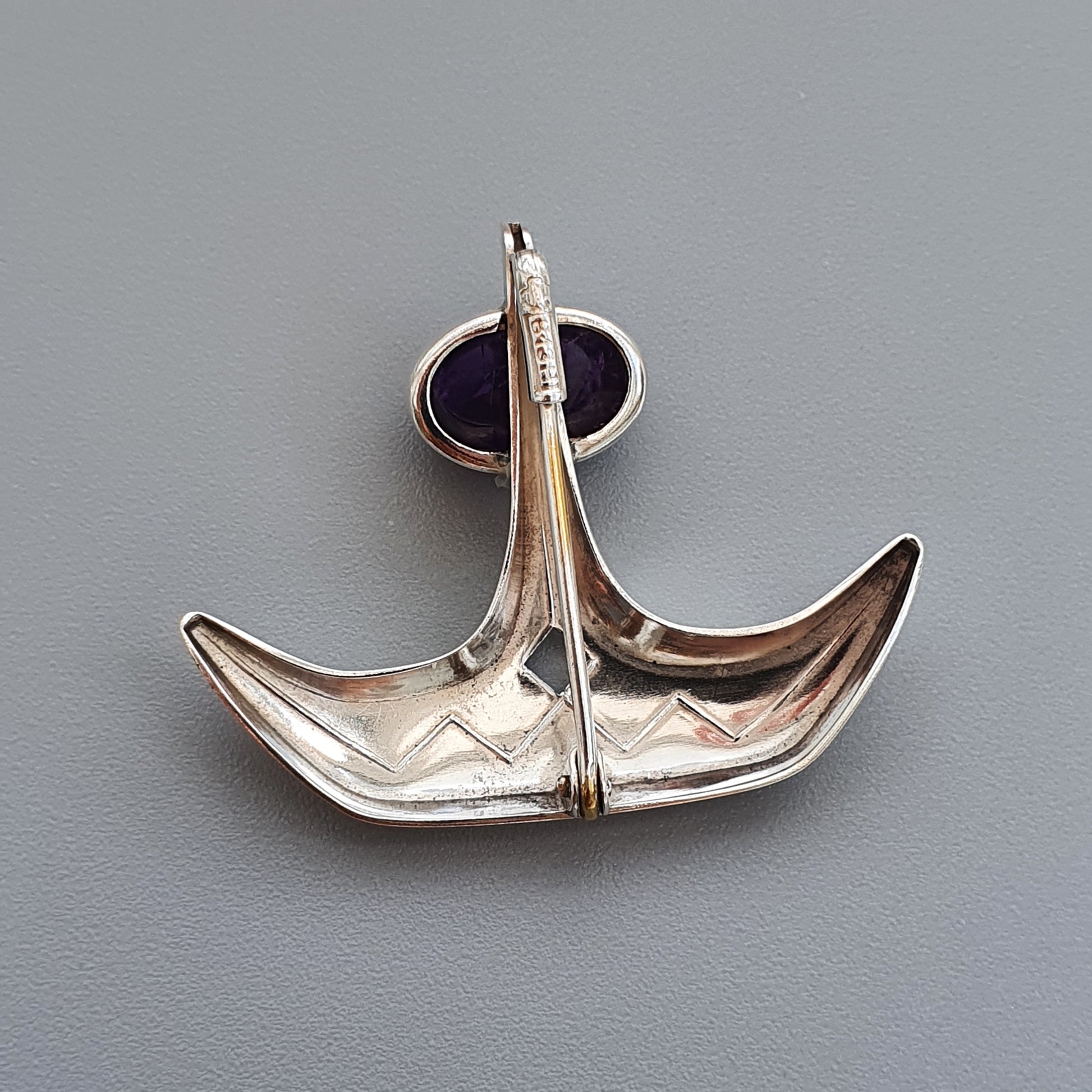 Silver pendant shaped like a stylized anchor or boat.