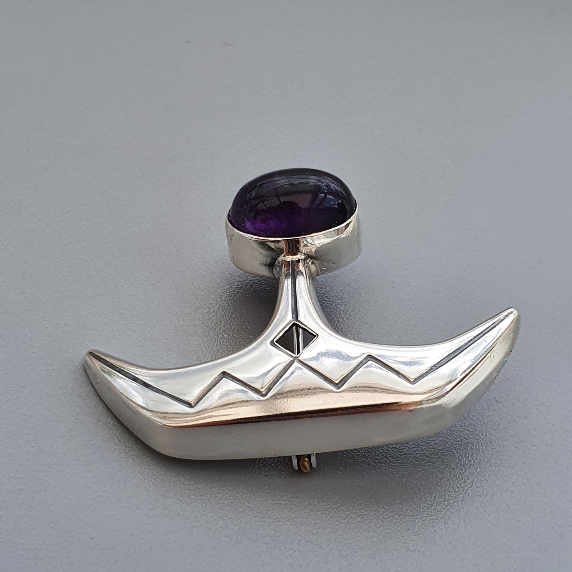 Silver pendant shaped like a stylized boat with a purple gemstone at the top.