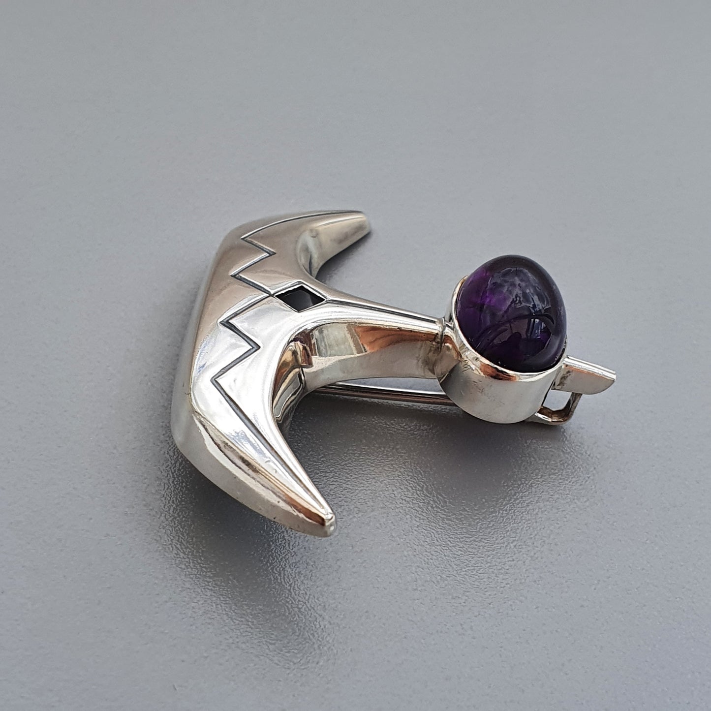 Silver crescent-shaped brooch or pin with a purple gemstone.